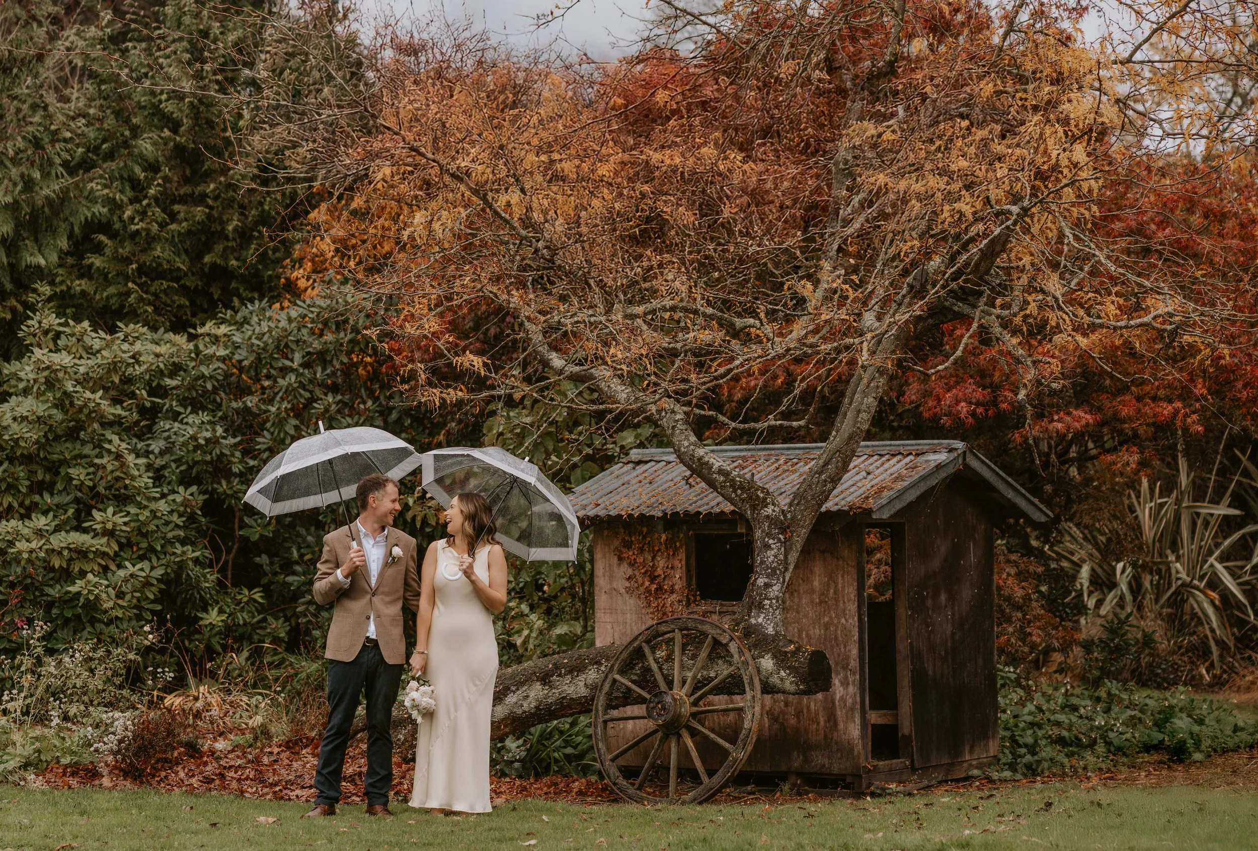 couple laugh under umbrellas during rainy elopement