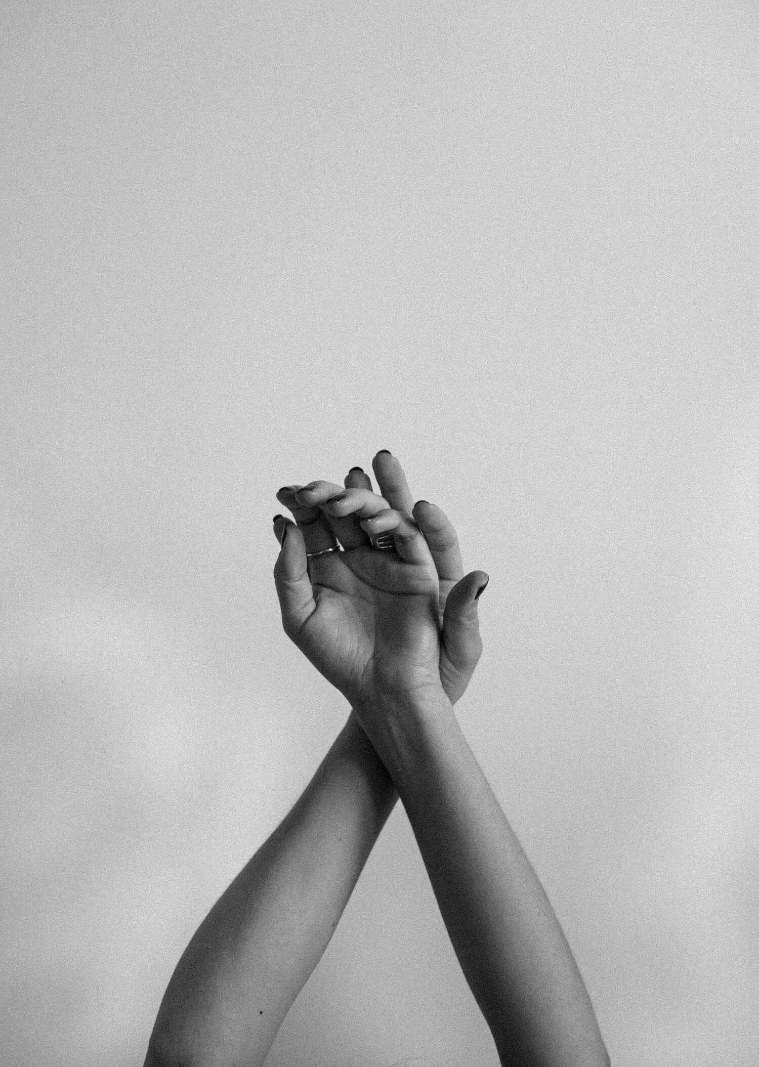 Two hands with fingers interlocked, raised against a plain light background.