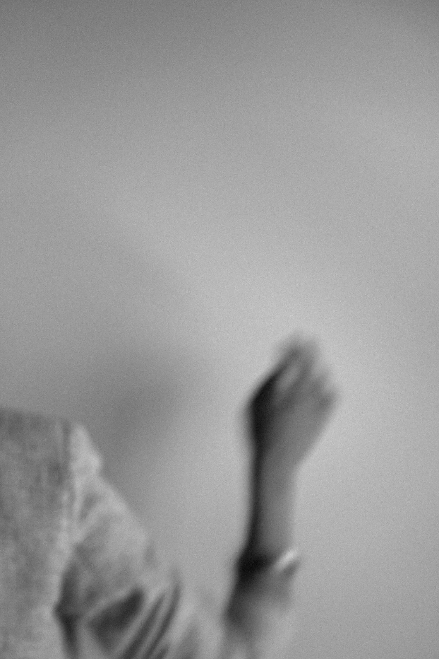 A blurred black-and-white photo of a person's hand and part of an arm, with a plain background.