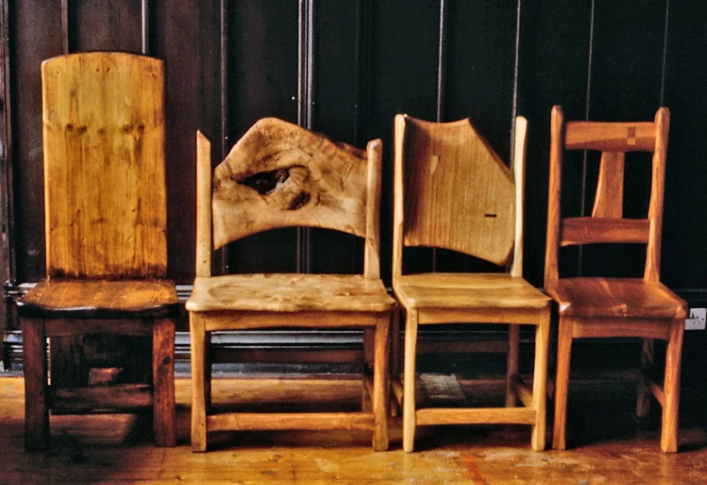 Four wooden chairs of different styles lined up against a dark wall.