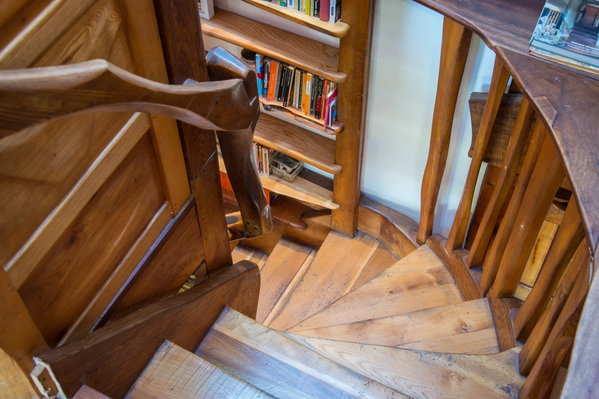 Wooden spiral staircase with a small bookshelf built into the wall, holding books and magazines.