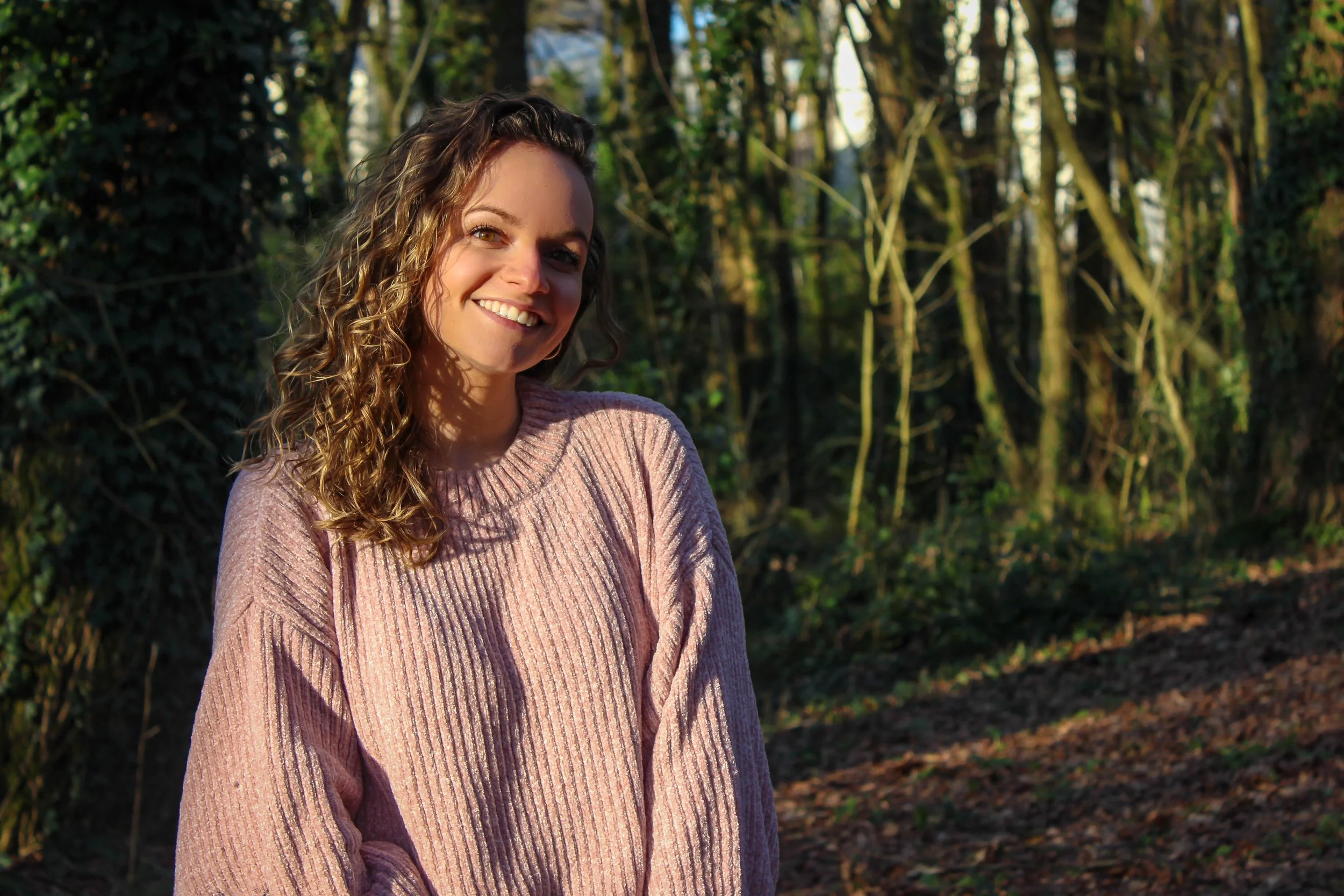 Femme souriante avec des cheveux bouclés dans une forêt.