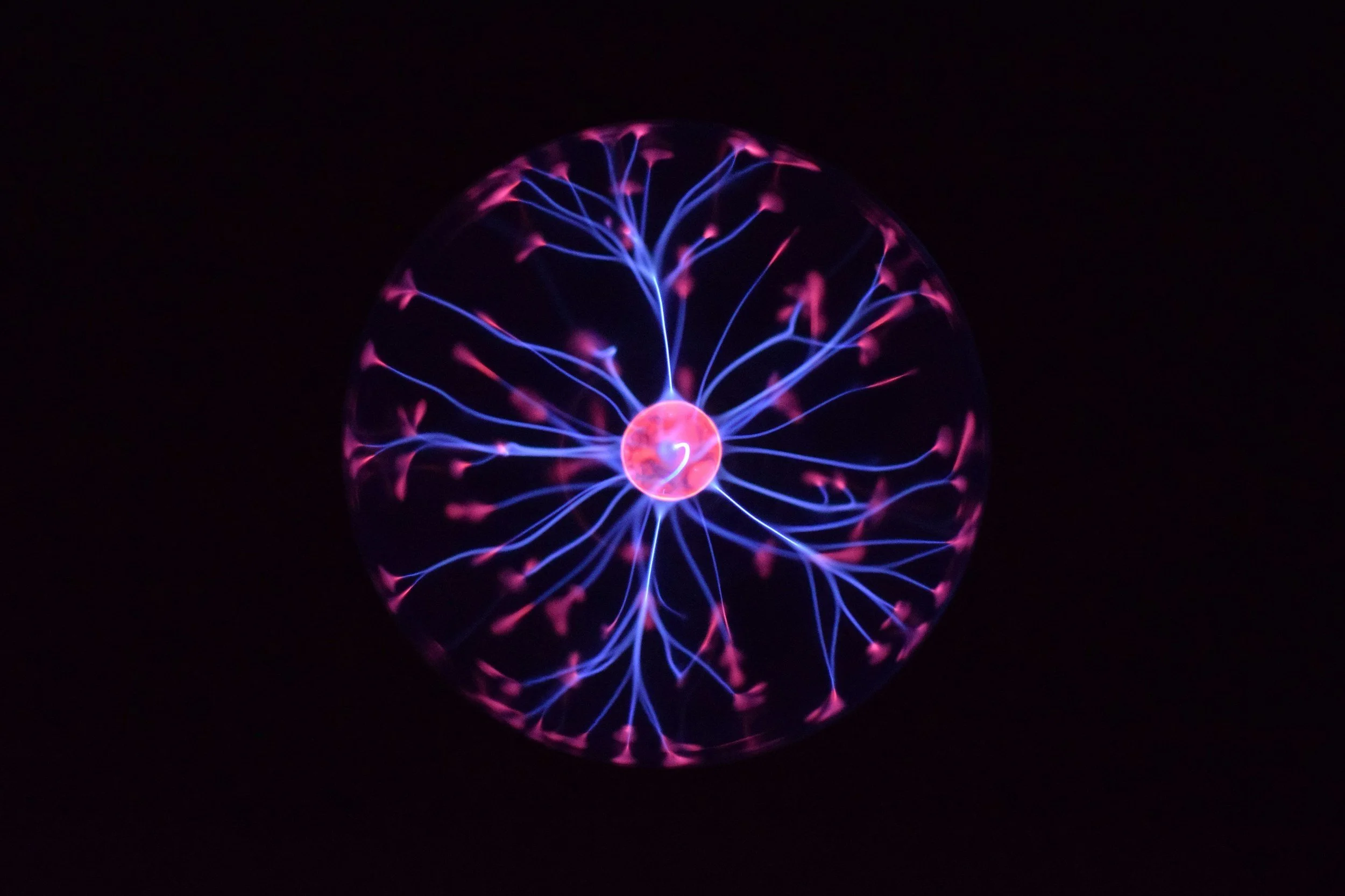 Close-up view of a plasma globe with blue and pink electric tendrils emanating from the center, against a black background.