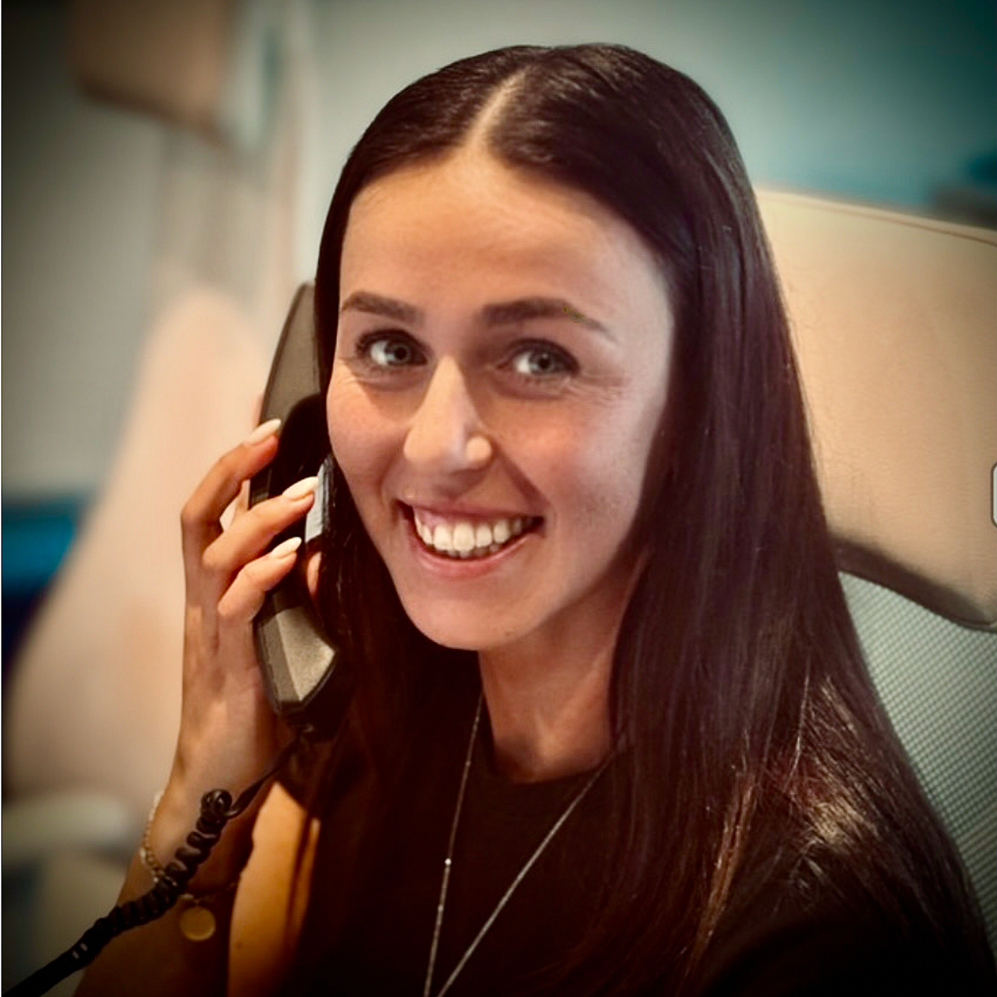 A woman with long dark hair smiling while talking on a landline phone.