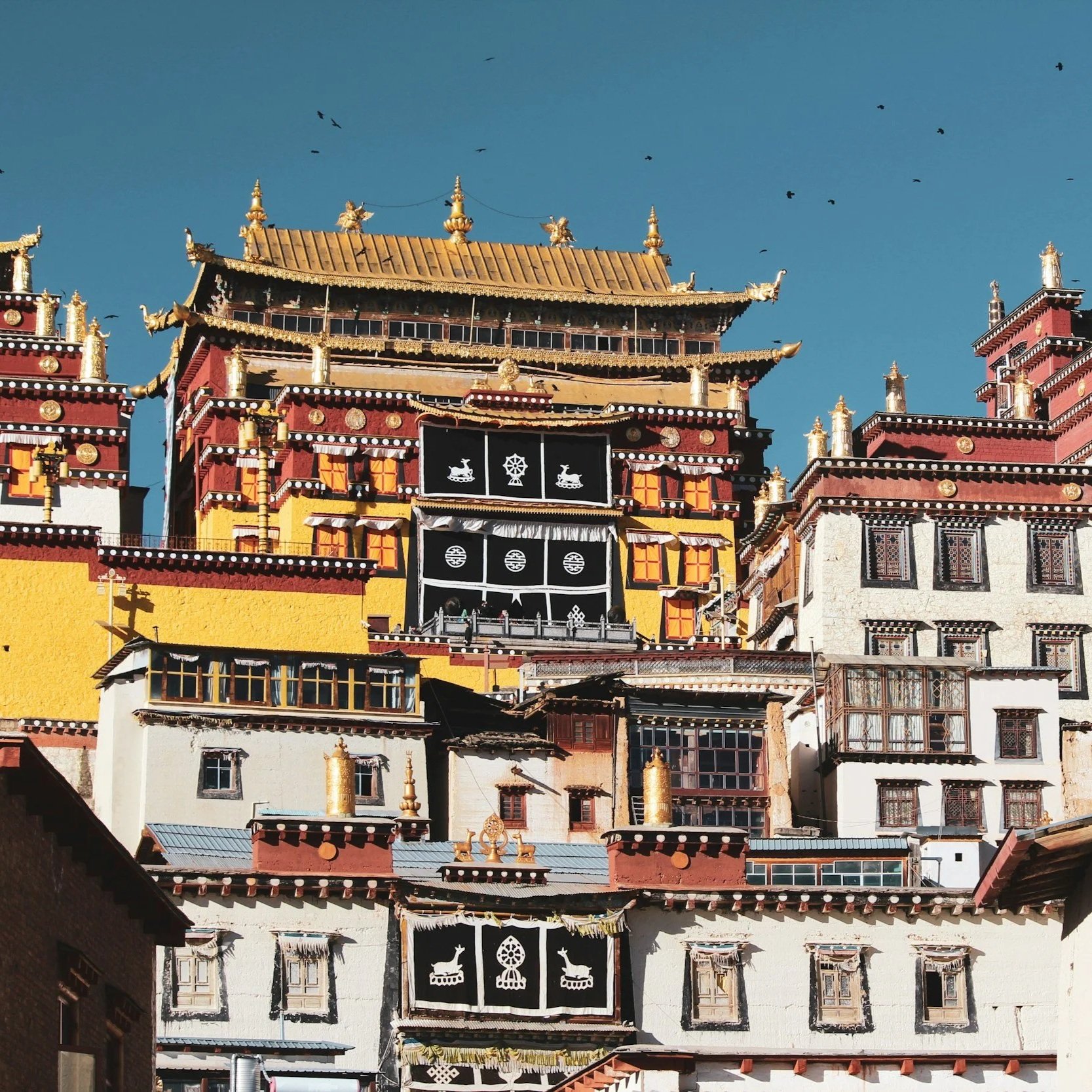 Colorful traditional Tibetan monastery with ornate architecture and prayer flags against a clear blue sky in Yunnan, China.