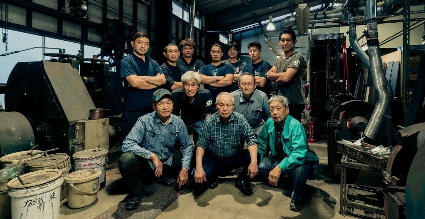 Master craftsmen and apprentices at Takefu Knife Village, Echizen, posing for a group photo in the workshop