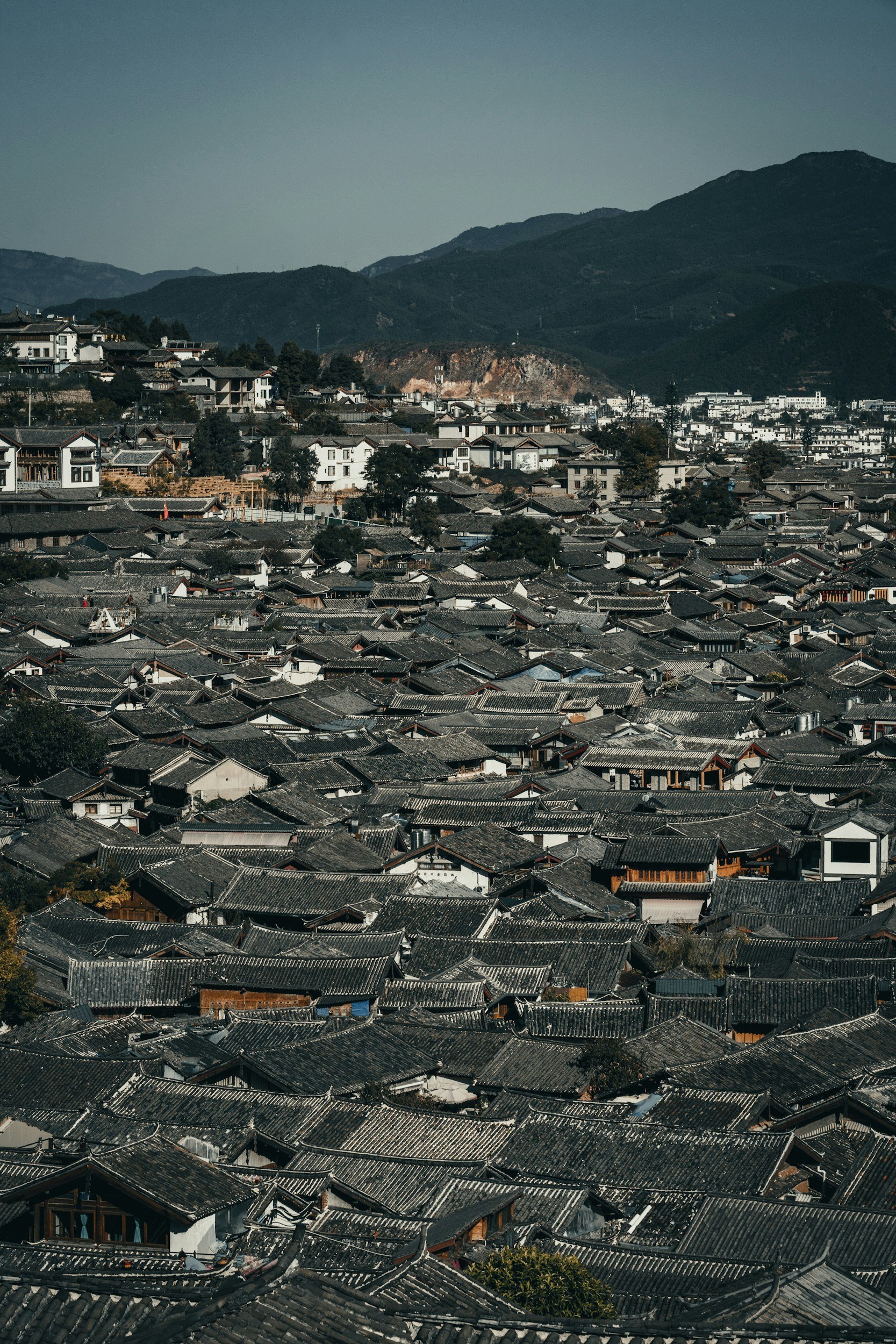 View of densely packed rooftops of Lijiang, Yunnan, China, set against a backdrop of mountains.
