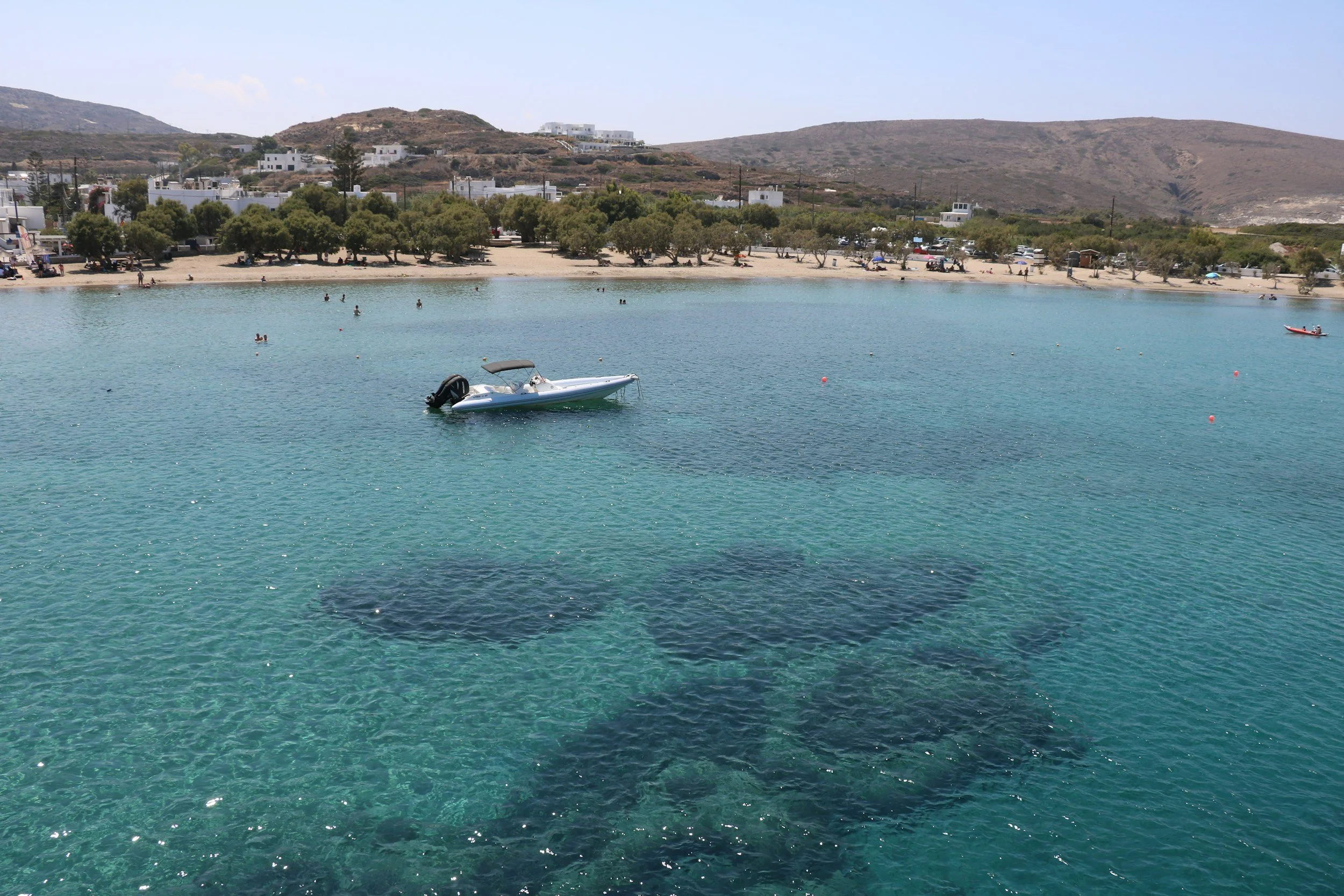 A boat on the water in a small harbour town, the beach in the background, and coral visible through the crystal clear water