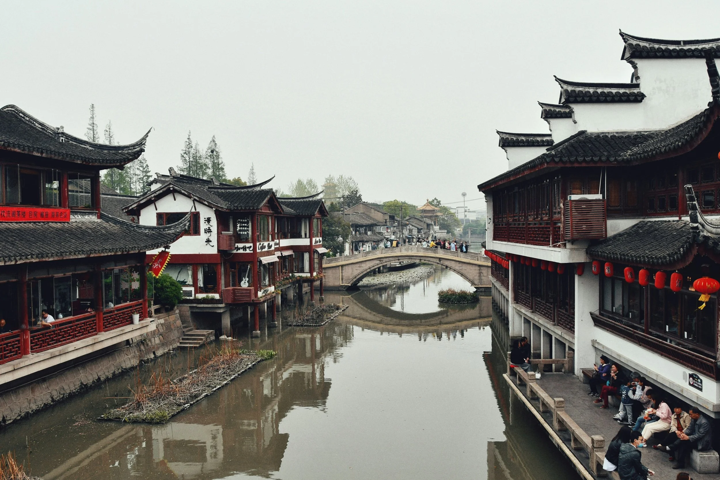 A canal in Shanghai's Qibao old town with traditional buildings on either side and a bridge reflecting in the water