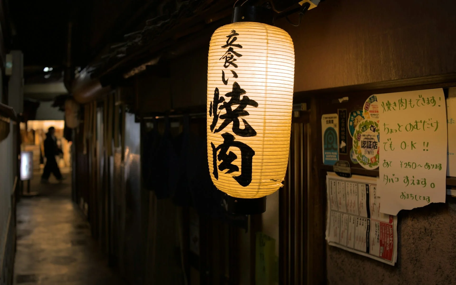 Glowing paper lantern reading "tachigui yakiniku" outside a Japanese restaurant alley at night