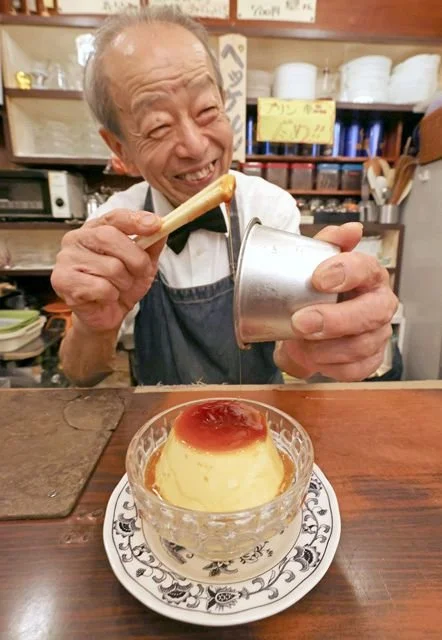 An old man at Hekkelun cafe in Tokyo smiling while he plates a homemade purin