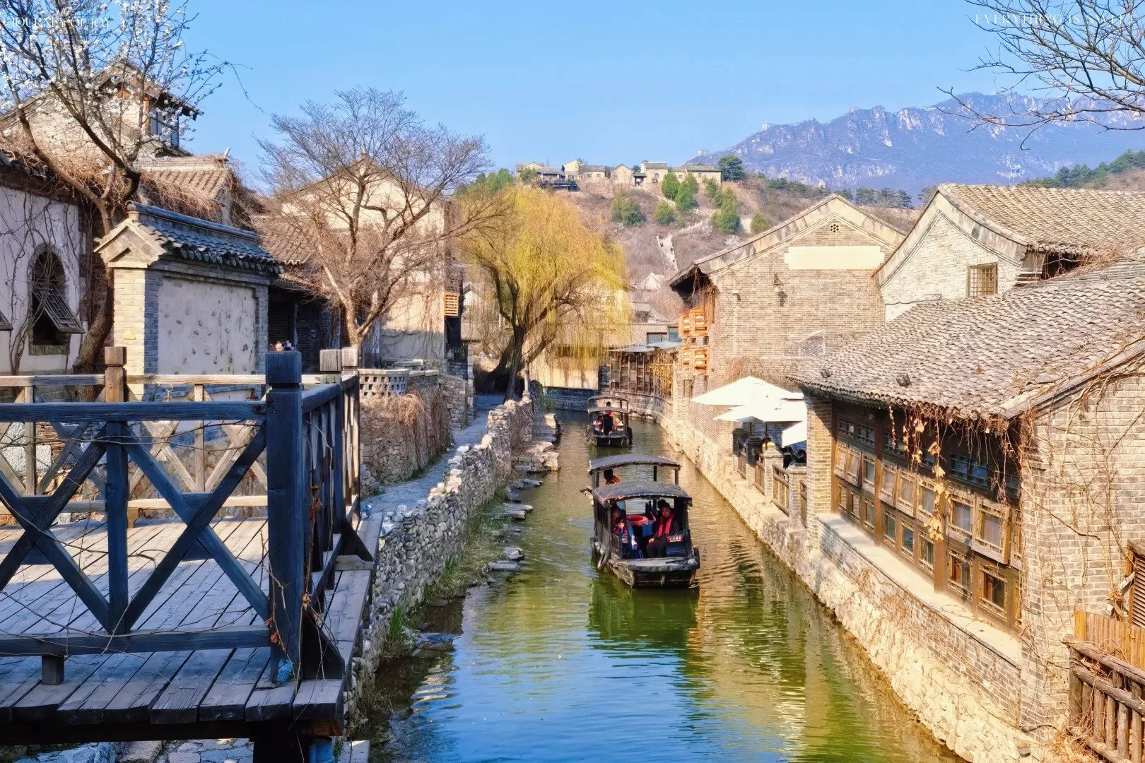 Traditional canal scene at Gubei Water Town with boats on the river and the Great Wall visible on the mountain ridgeline above, Miyun District Beijing