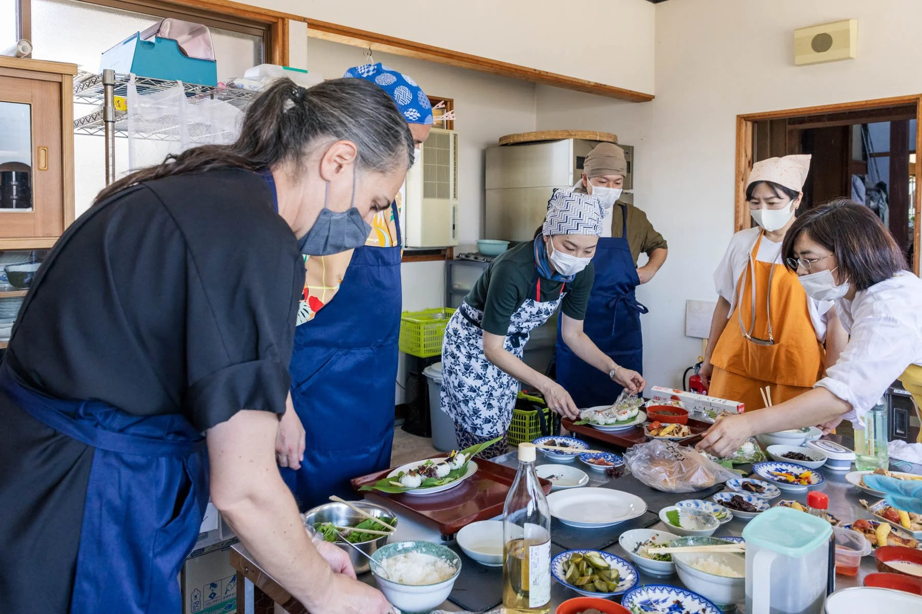A group of people gathered around a table taking a Japanese cooking class, and the table is laid with many small plates of ingredients and pickles