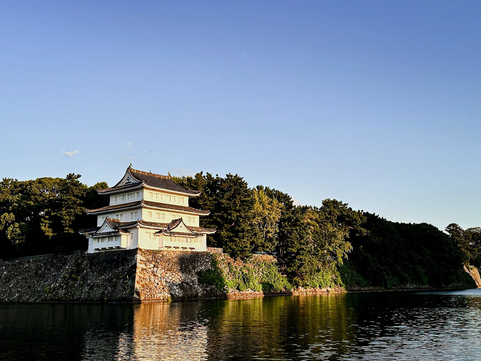 A tower at the edge of Nagoya castle, surrounded by trees and reflected in the moat