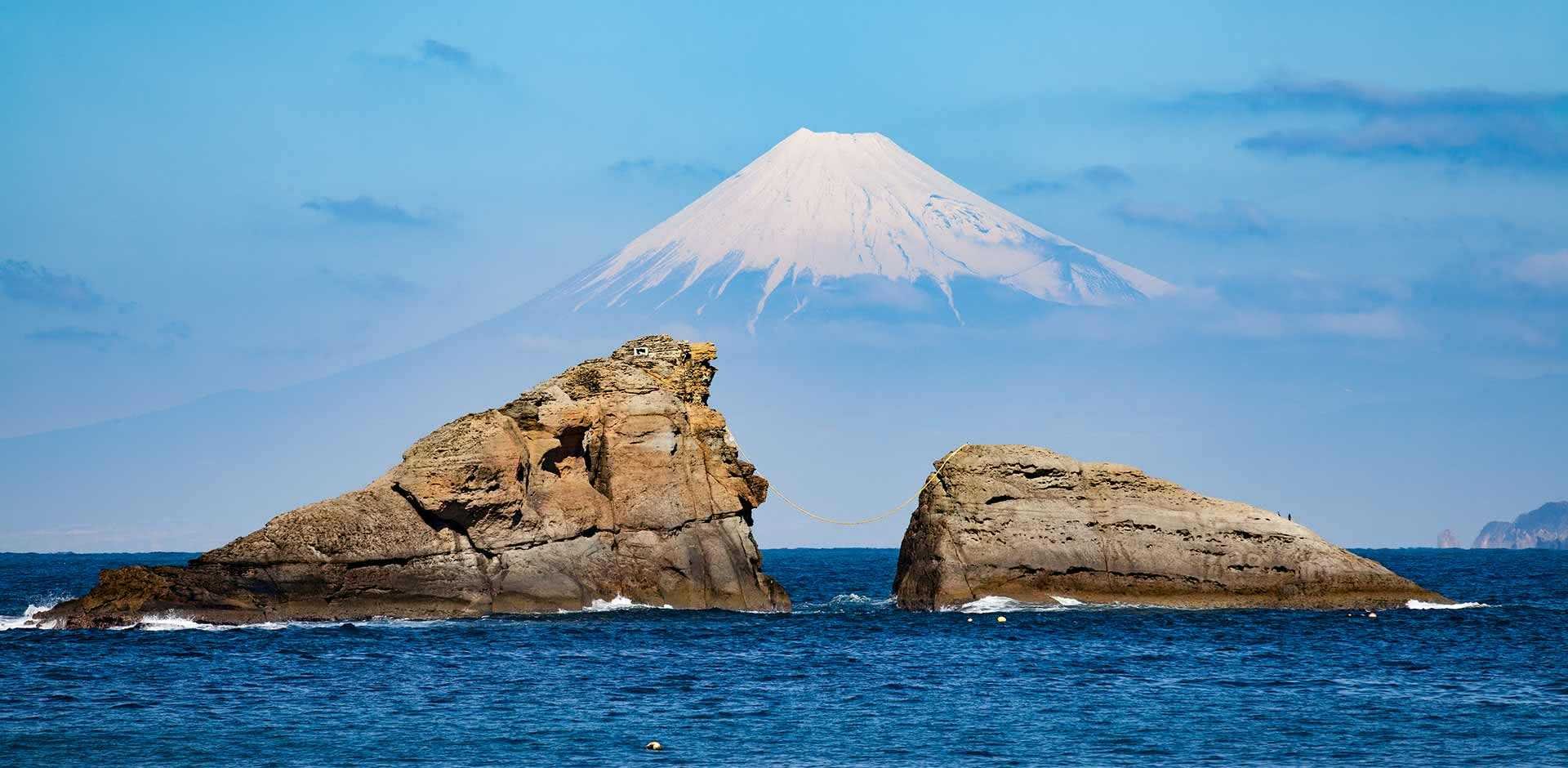 Two rocks on the coastline of the Izu Peninsula jutting out of the sea, with Mount Fuji in the background