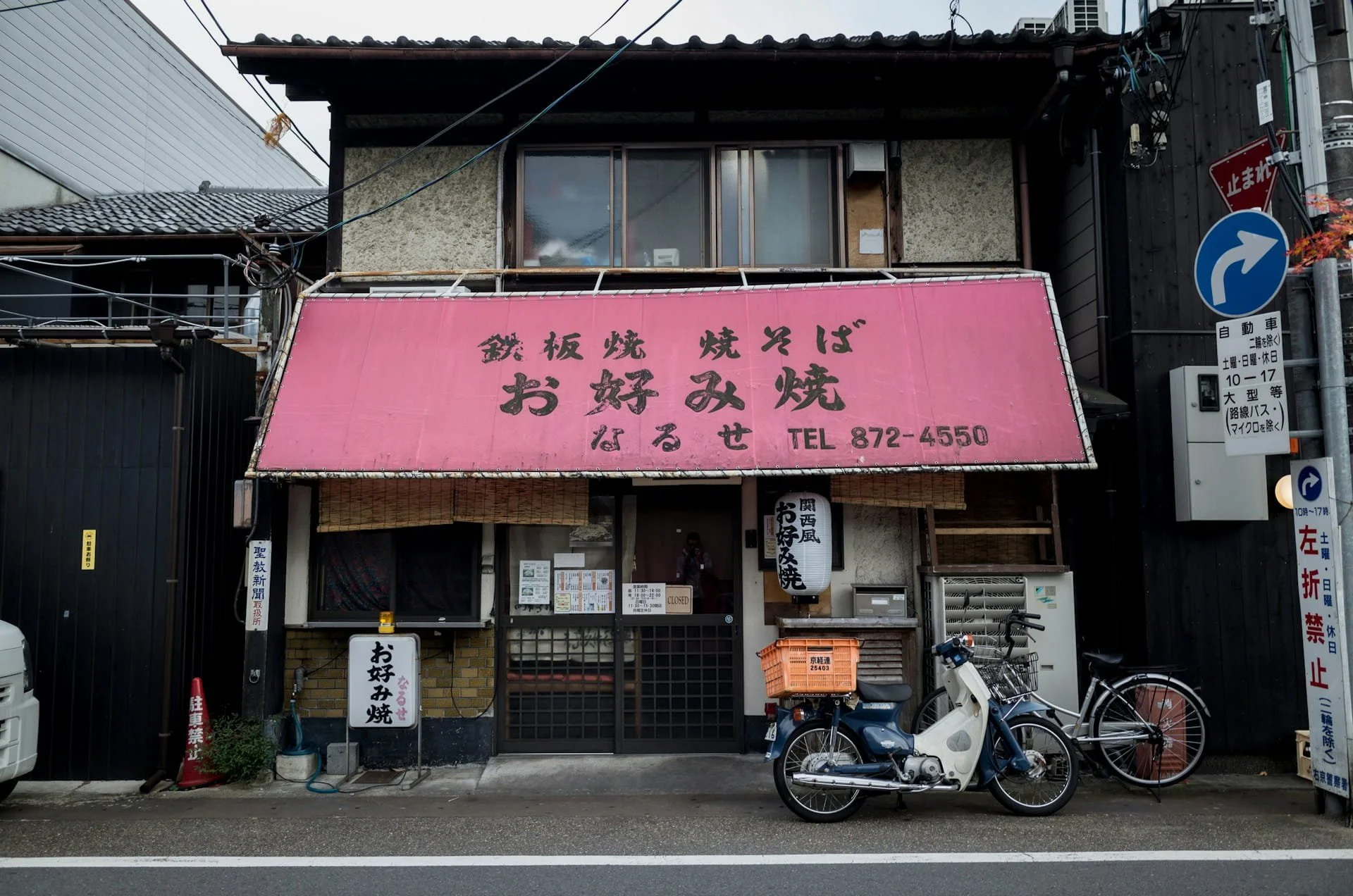 Faded pink shopfront of a traditional okonomiyaki restaurant in Japan, with a moped parked outside