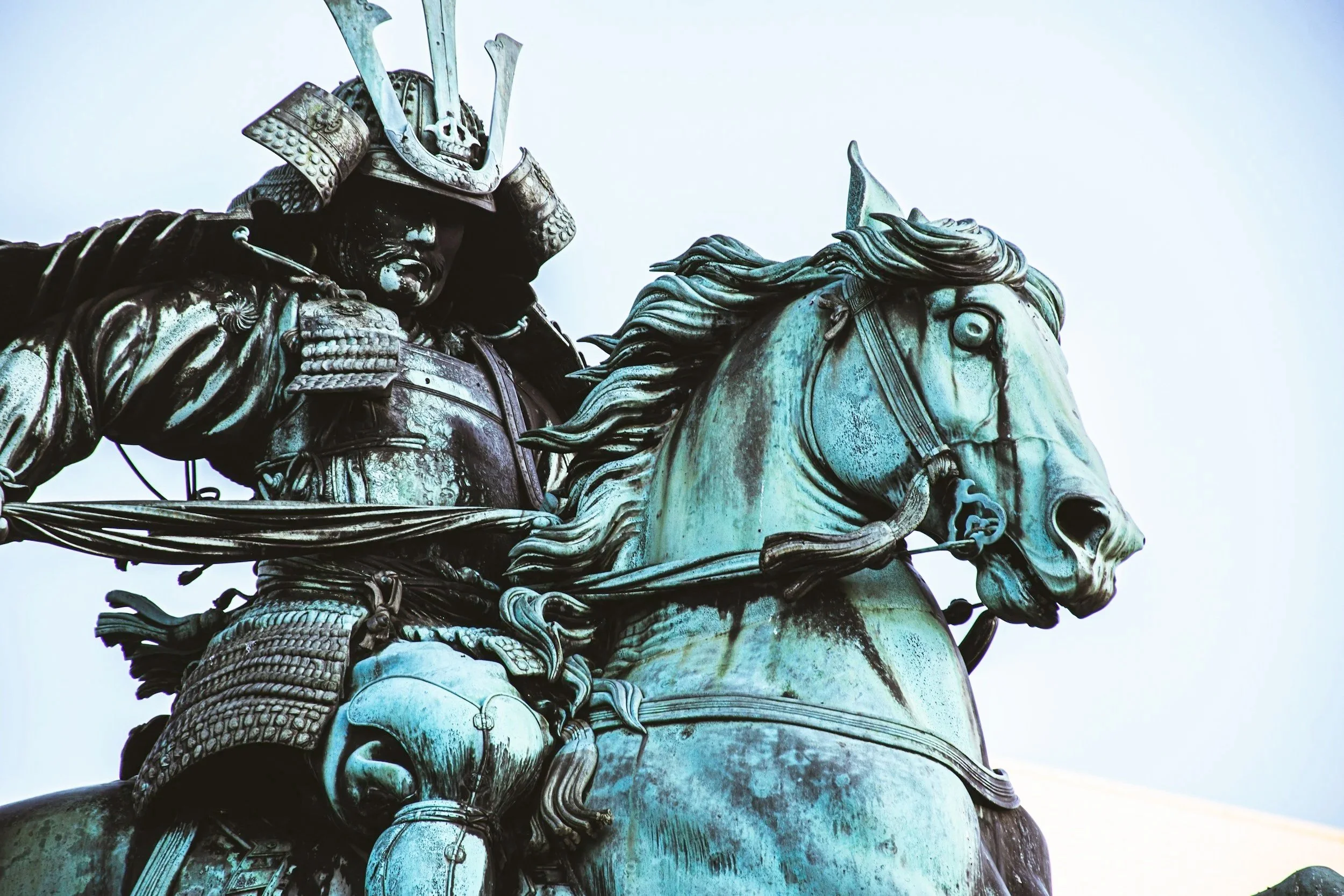 Close-up of a bronze statue of a samurai warrior on horseback, wearing traditional armor and helmet, with intricate detailing.