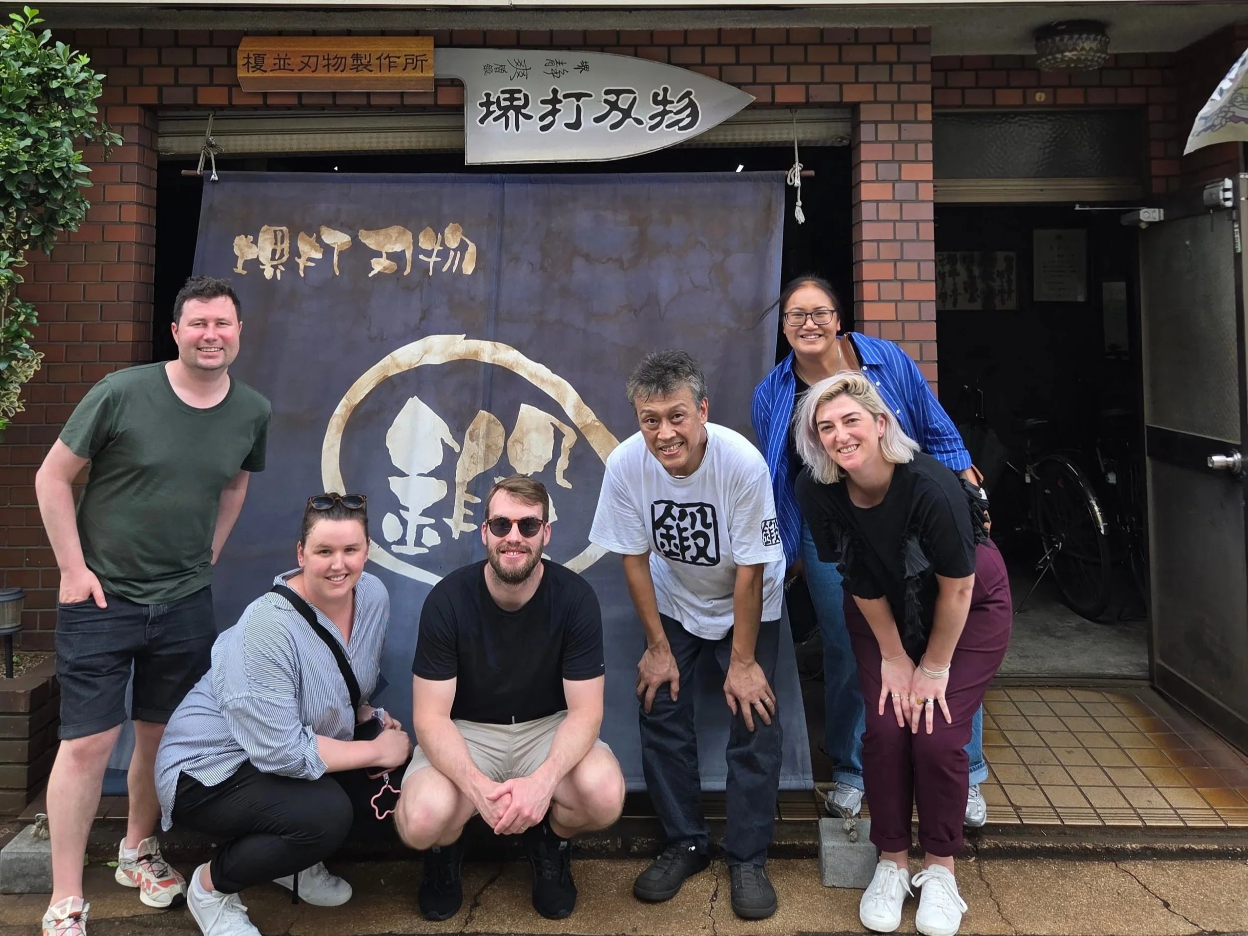 Group of visitors outside Enami Cutlery Factory in Sakai, with the workshop's noren curtain and sign