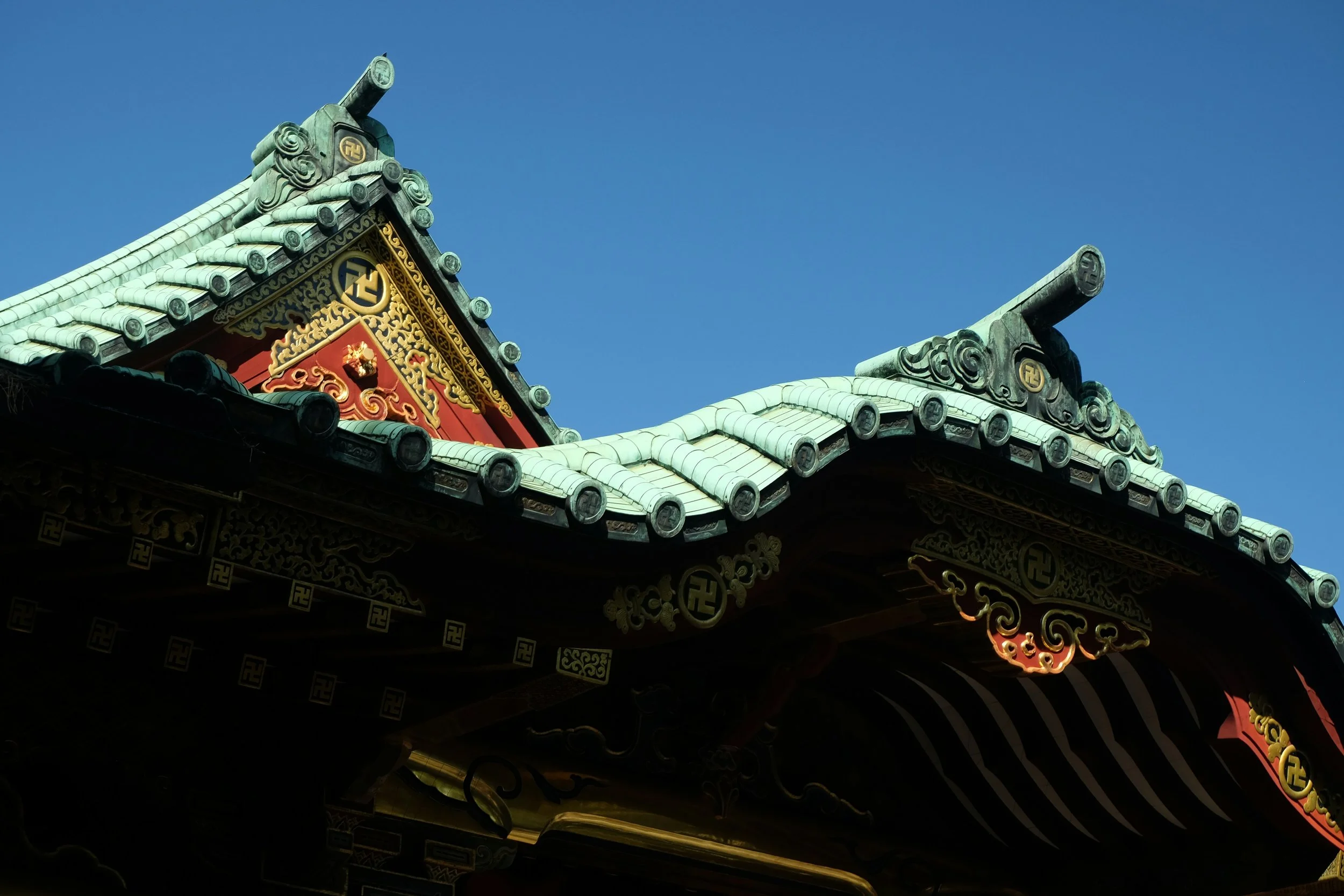 Close-up of traditional Japanese temple roof at Hiraizumi in Iwate with ornate decorations, gold accents, and a clear blue sky in the background.