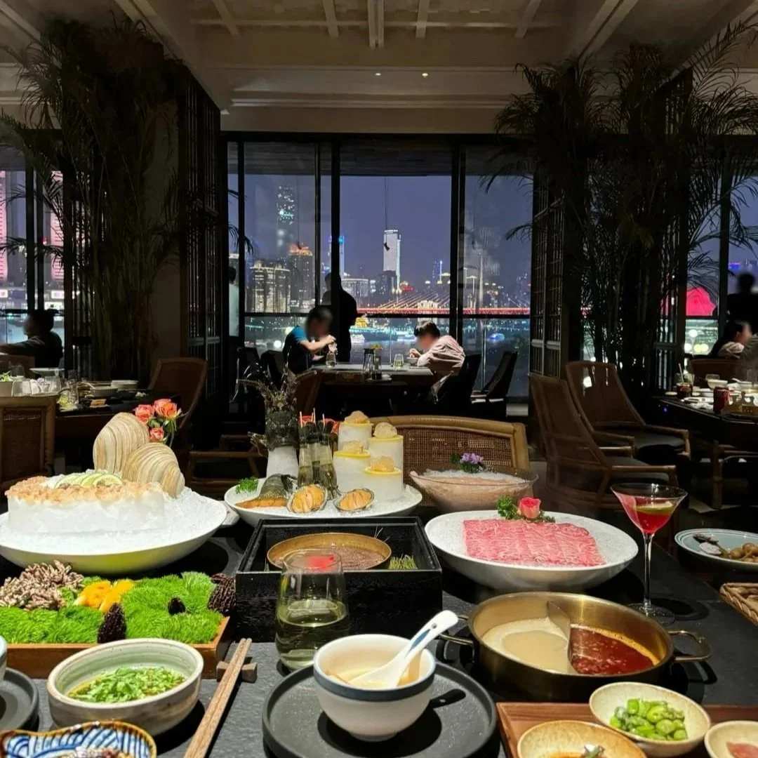 Upscale hot pot spread at 滟设 restaurant in Chongqing, with the city skyline visible through floor-to-ceiling windows at night