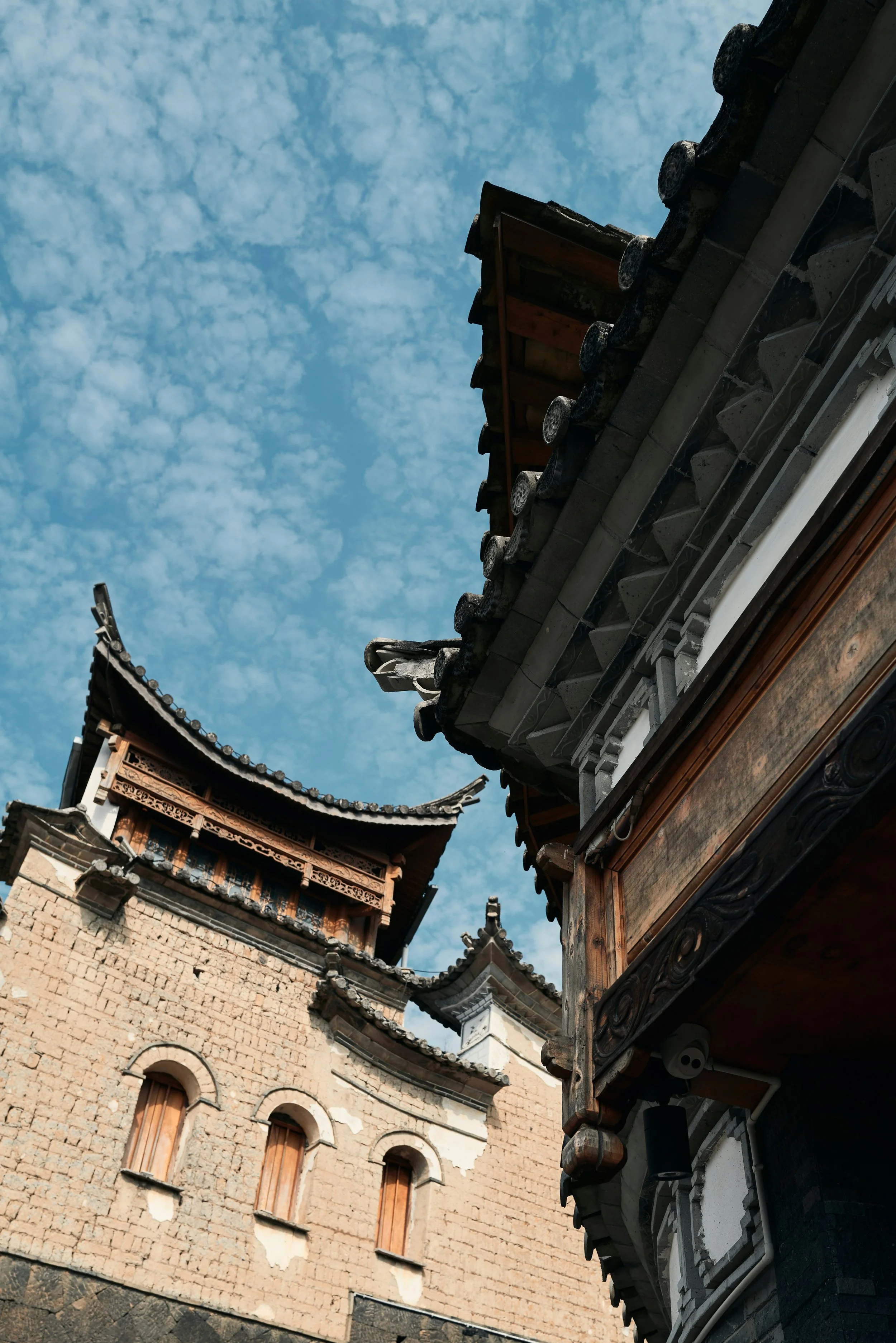 Traditional Asian-style building rooftops with ornate details, against a blue sky with scattered clouds in southern Yunnan.