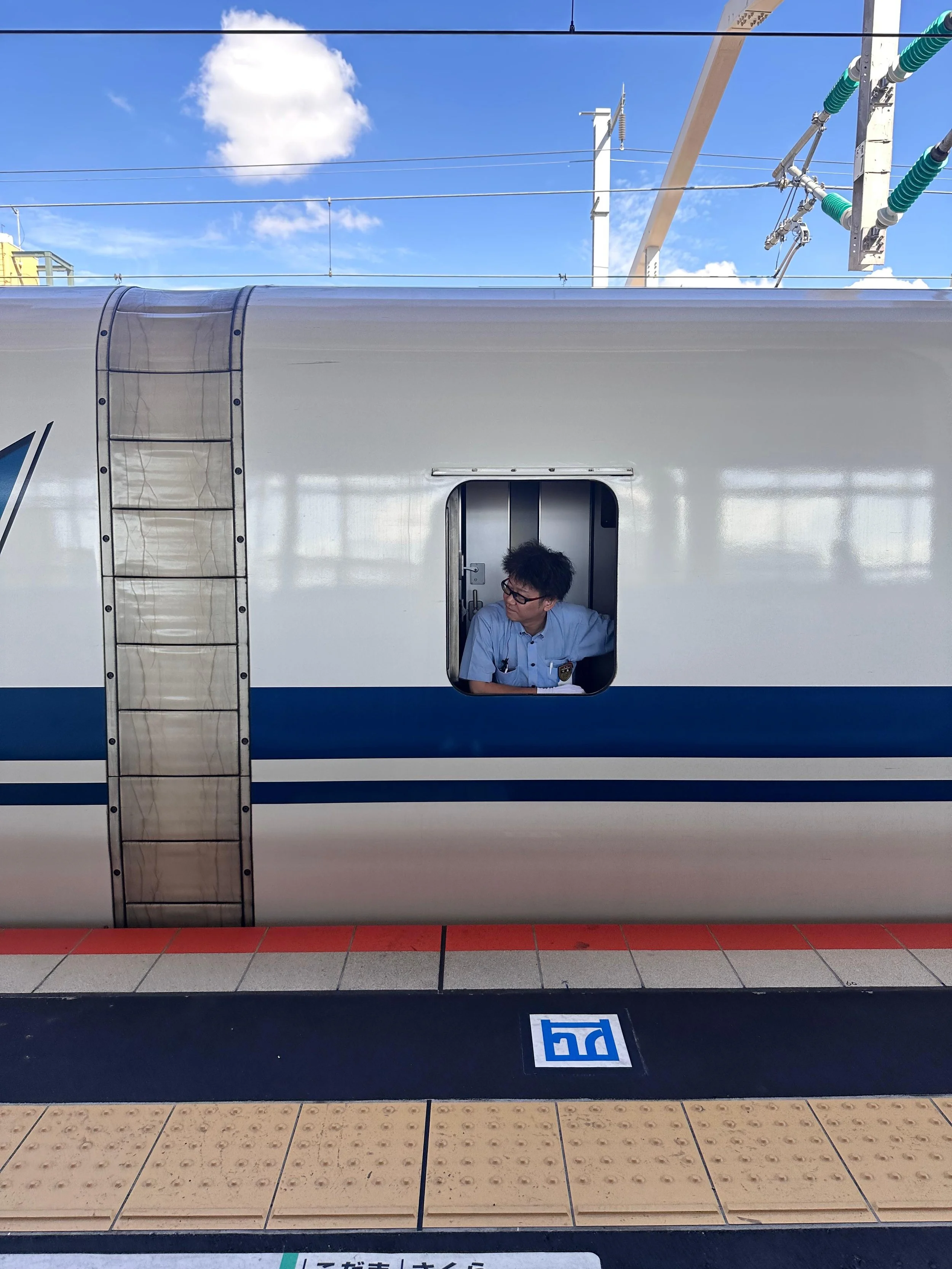 A train conductor on a Shinkansen, poking his head out the window to check if the platform is clear before departure