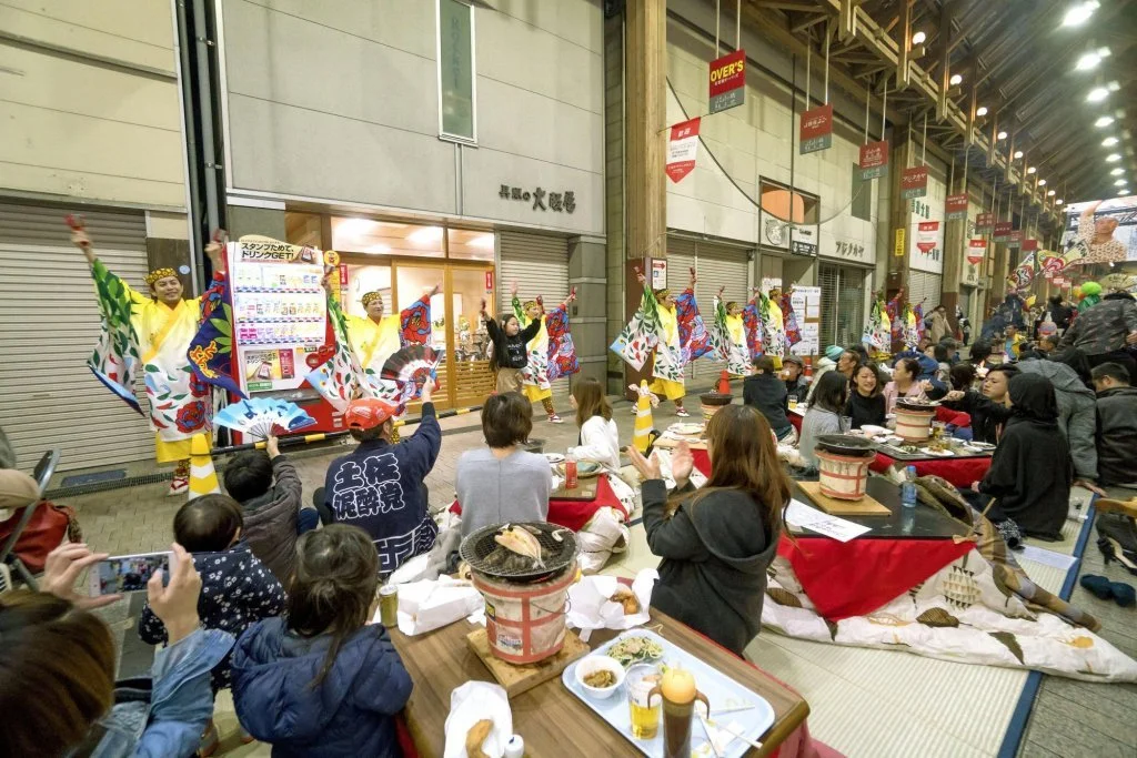 crowds of people sitting on the street around tables, celebrating the Tosa no Okyaku festival with food and drink