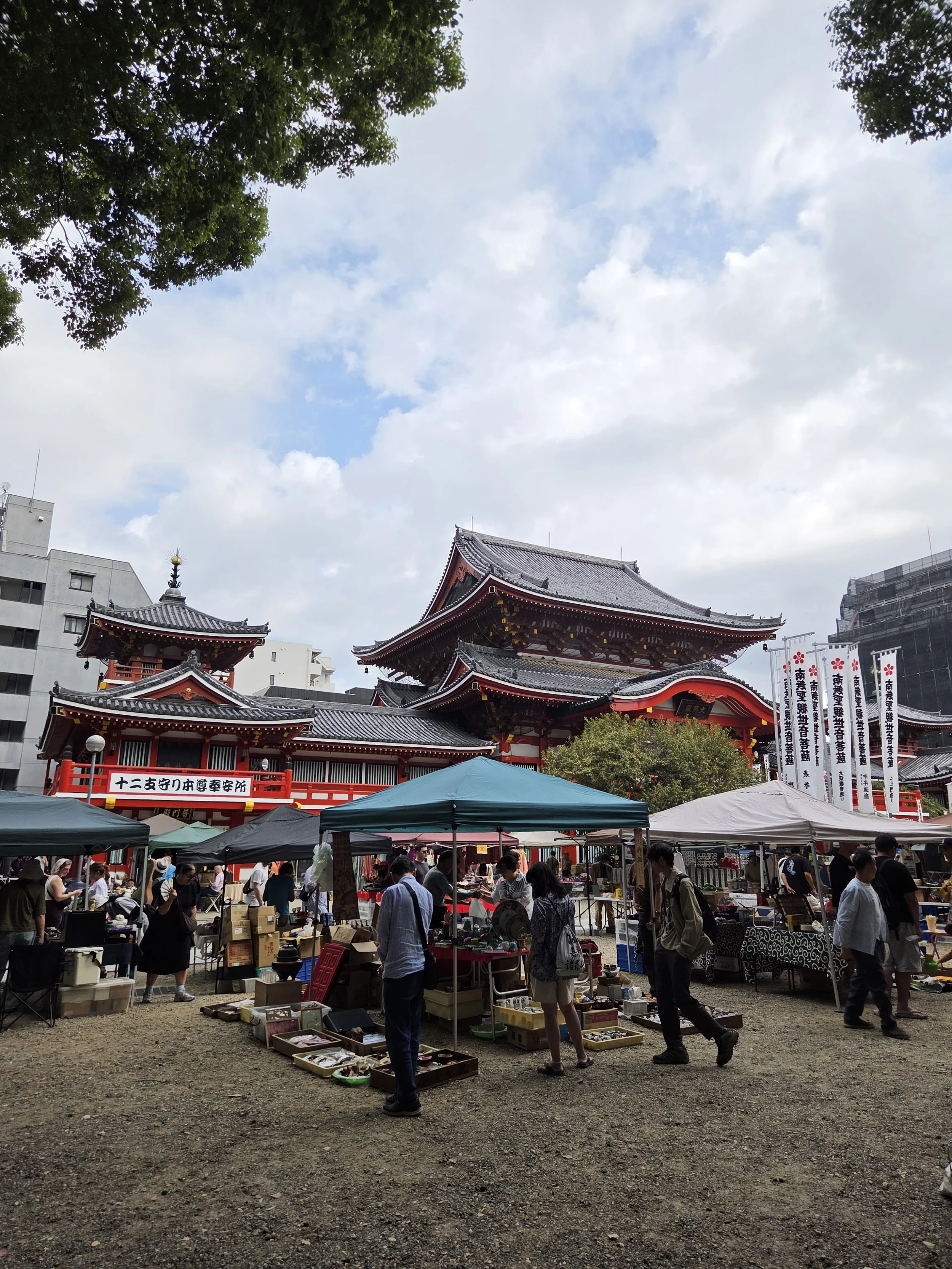 People shopping for antiques and knick knacks at a market with many marquees in front of a traditional Japanese temple