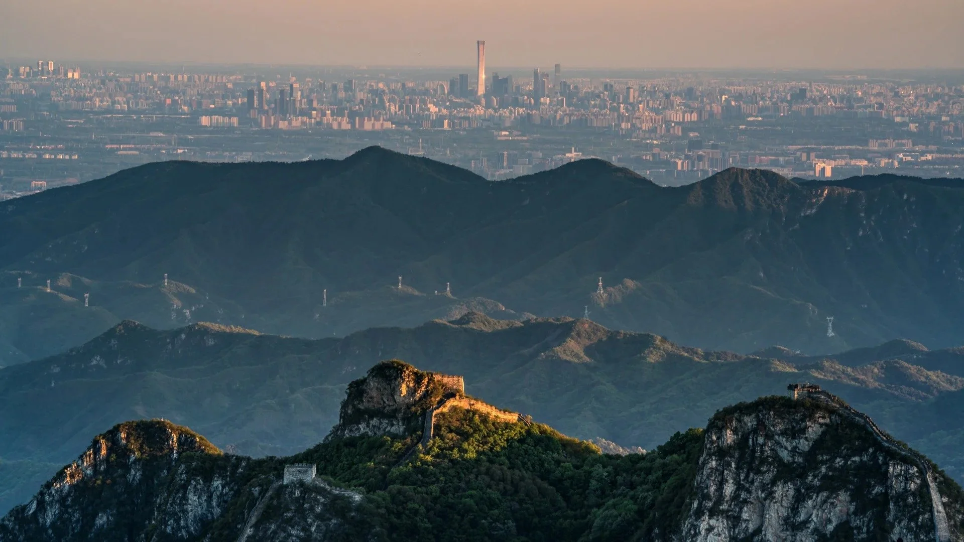 Jiankou Great Wall watchtowers on rocky peaks near Beijing, with the city skyline visible through haze in the background