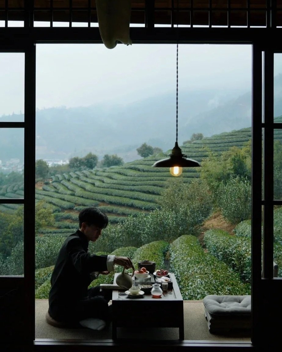 A man pouring himself tea on a balcony in front of a tea plantation in Wuyi Shan