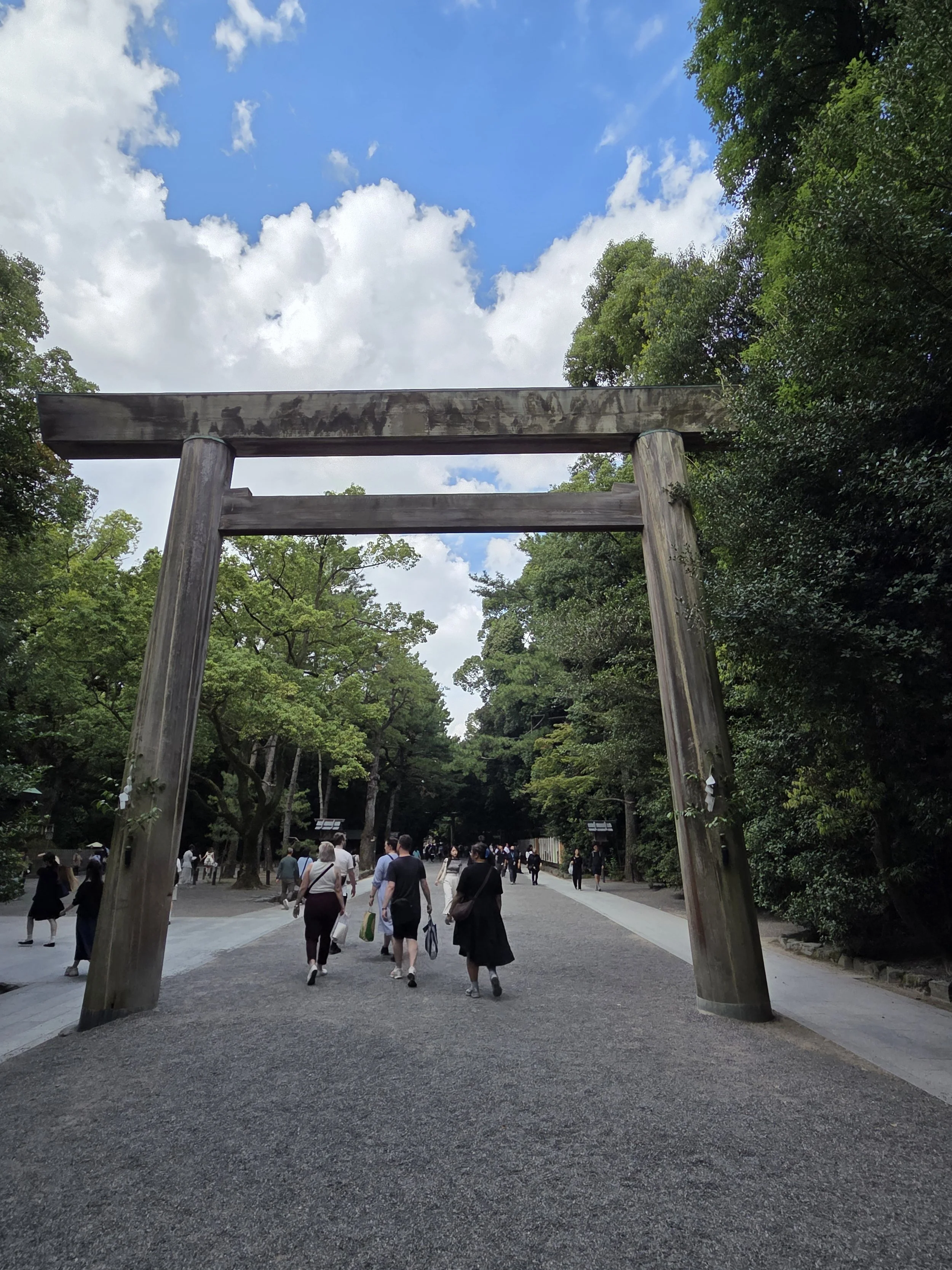 A group of people walking under a large torii and entering the grounds of Atsuta-jingu in Nagoya, an oasis in the middle of the city