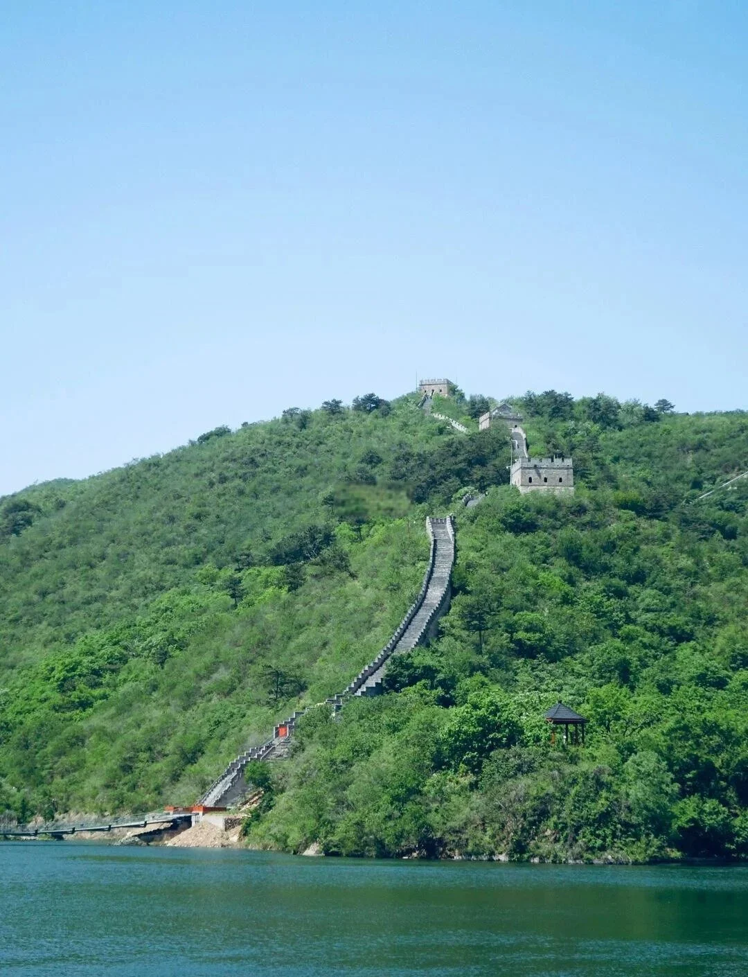 Huanghuacheng Great Wall descending a green hillside straight into the reservoir below, watchtowers visible above the waterline, Huairou District Beijing