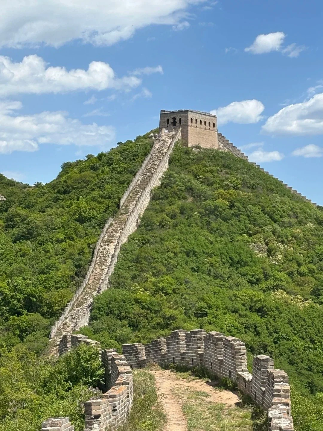 Looking up at an unrestored Ming dynasty watchtower at Shixiaguan Great Wall, the wall climbing steeply through green forest at Shixiaguan near Badaling, Beijing