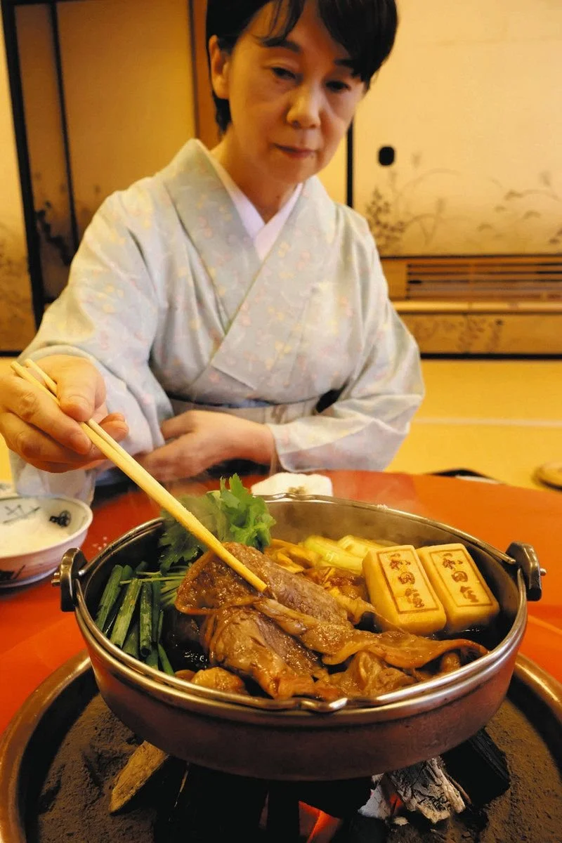 Wagyu sukiyaki prepared tableside by a kimono-clad host in a traditional Japanese dining room
