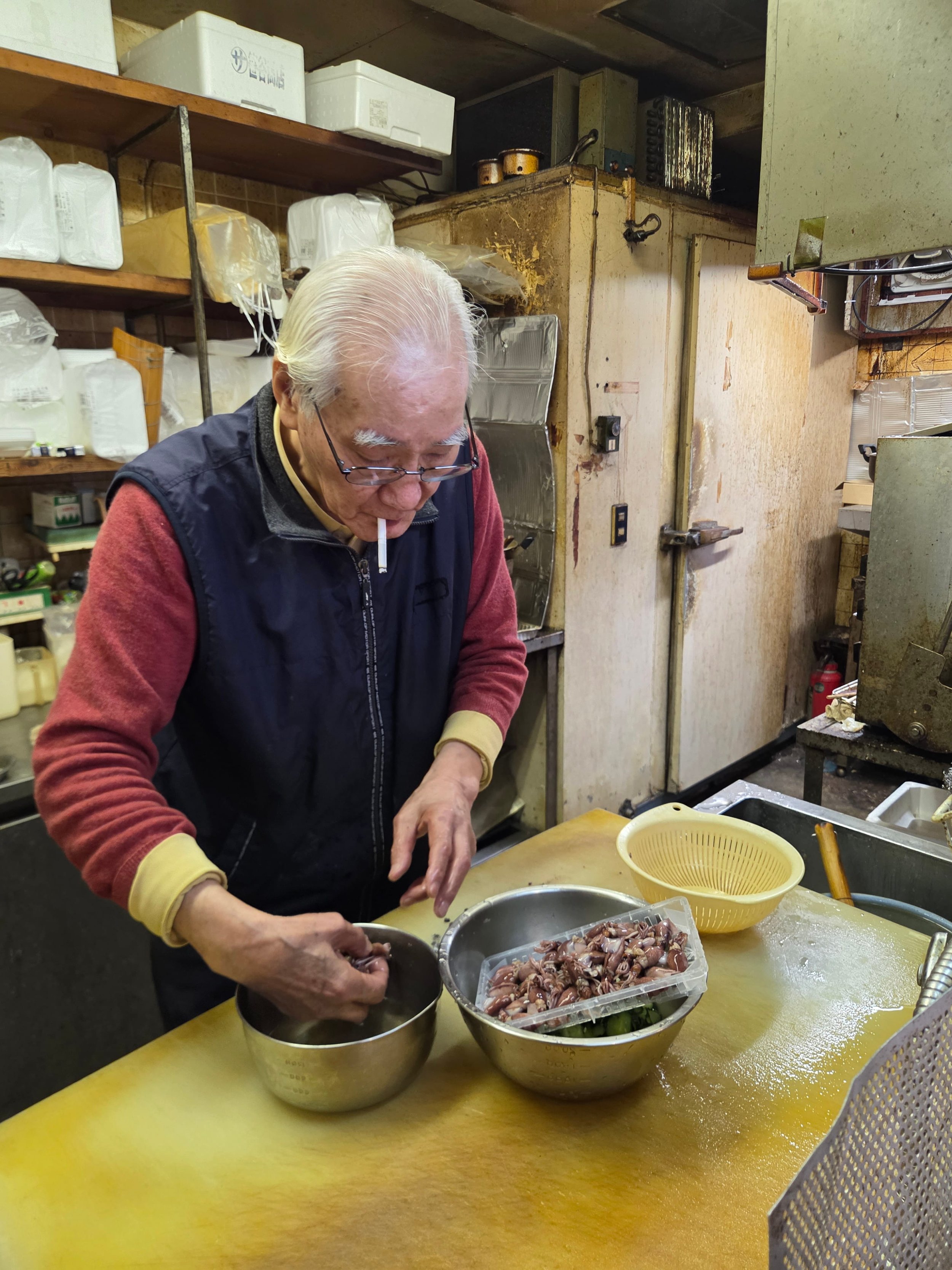 Elderly Japanese chef preparing food with a cigarette in his mouth in a worn kitchen — a quintessential Dirty Michelin scene