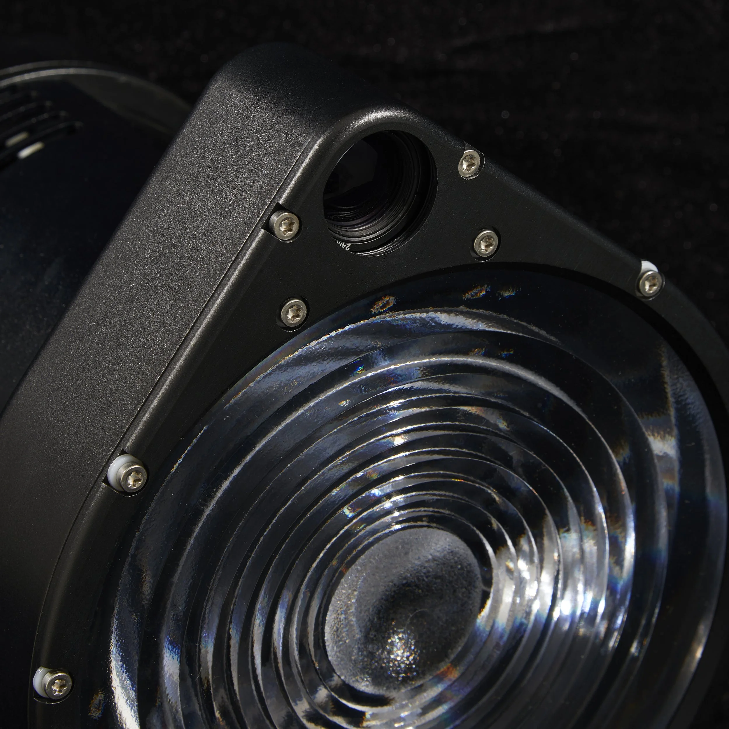 Close-up of a black speaker with a shiny, concentric circular grill and a small, dark port at the top.
