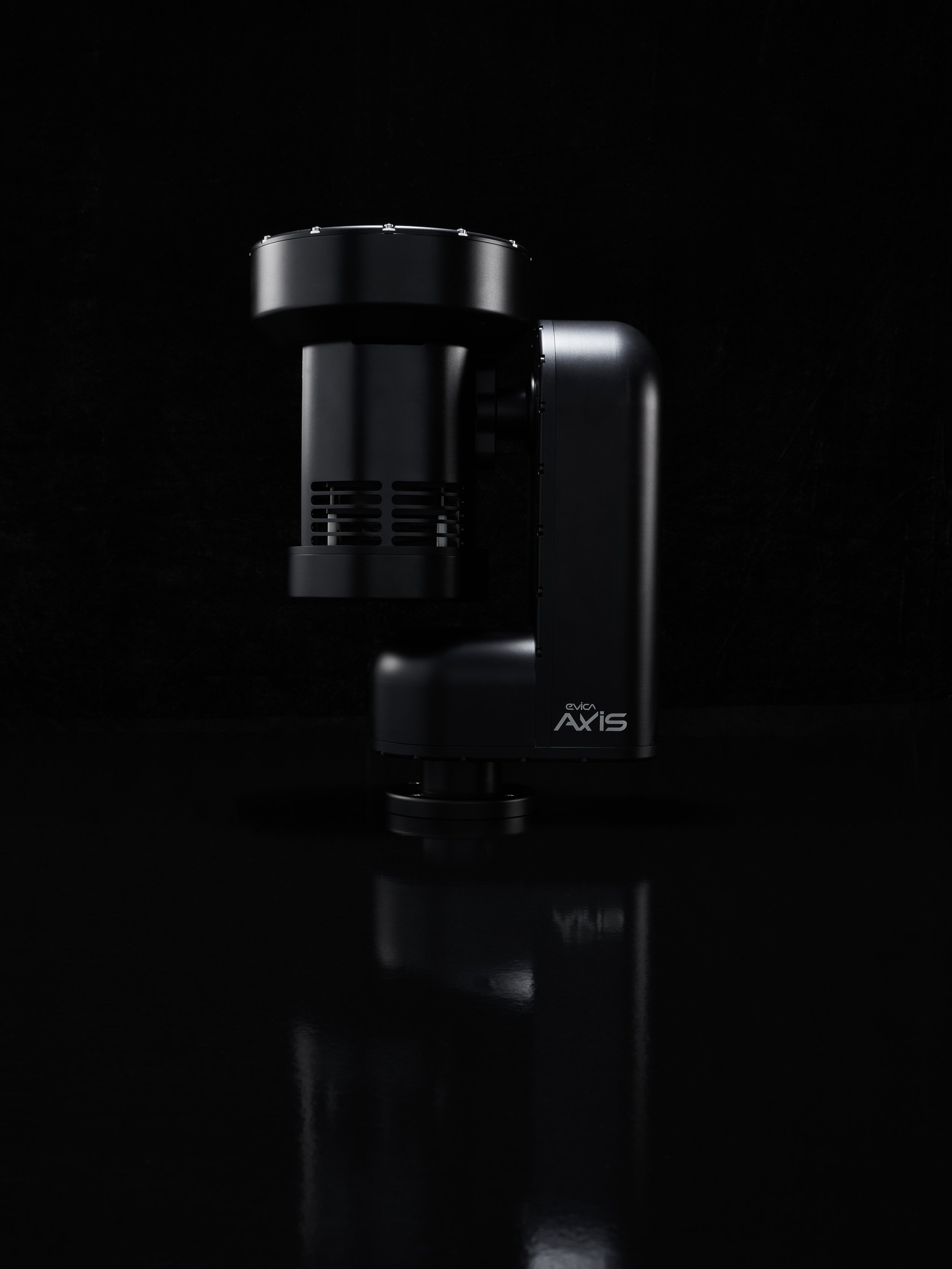 Black robotic arm or machine with a sleek design, set against a dark background, with faint reflections on the surface below.