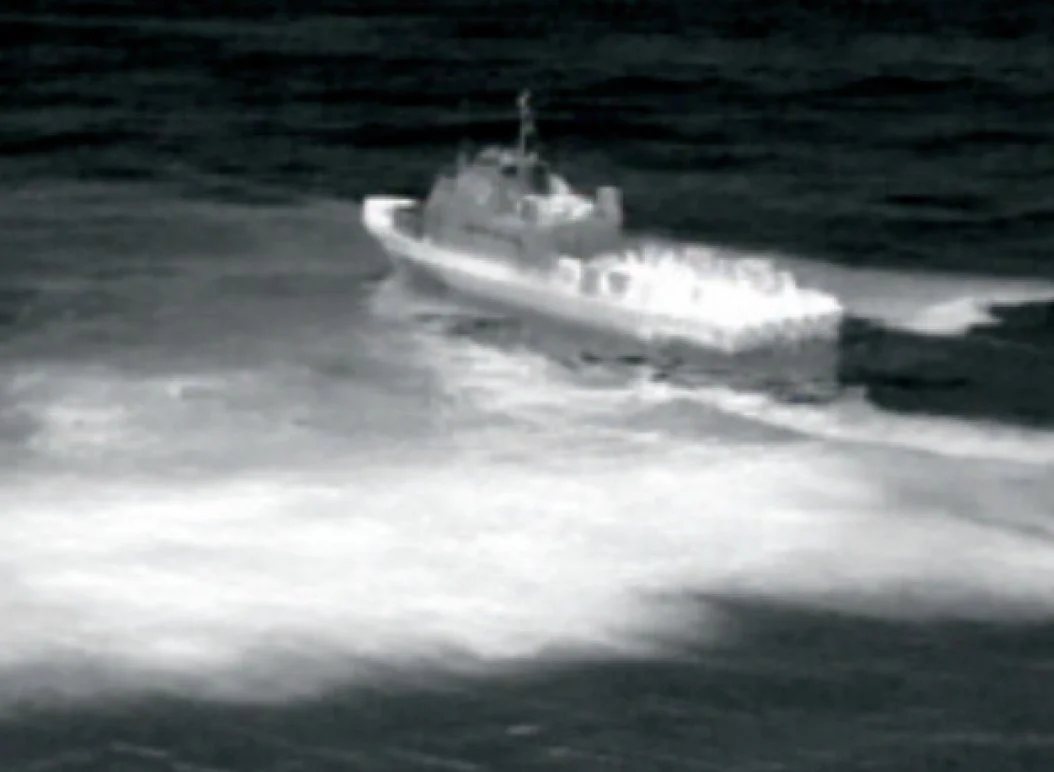 A grayscale image of a boat moving across the water, leaving a wake behind, on a dark ocean.