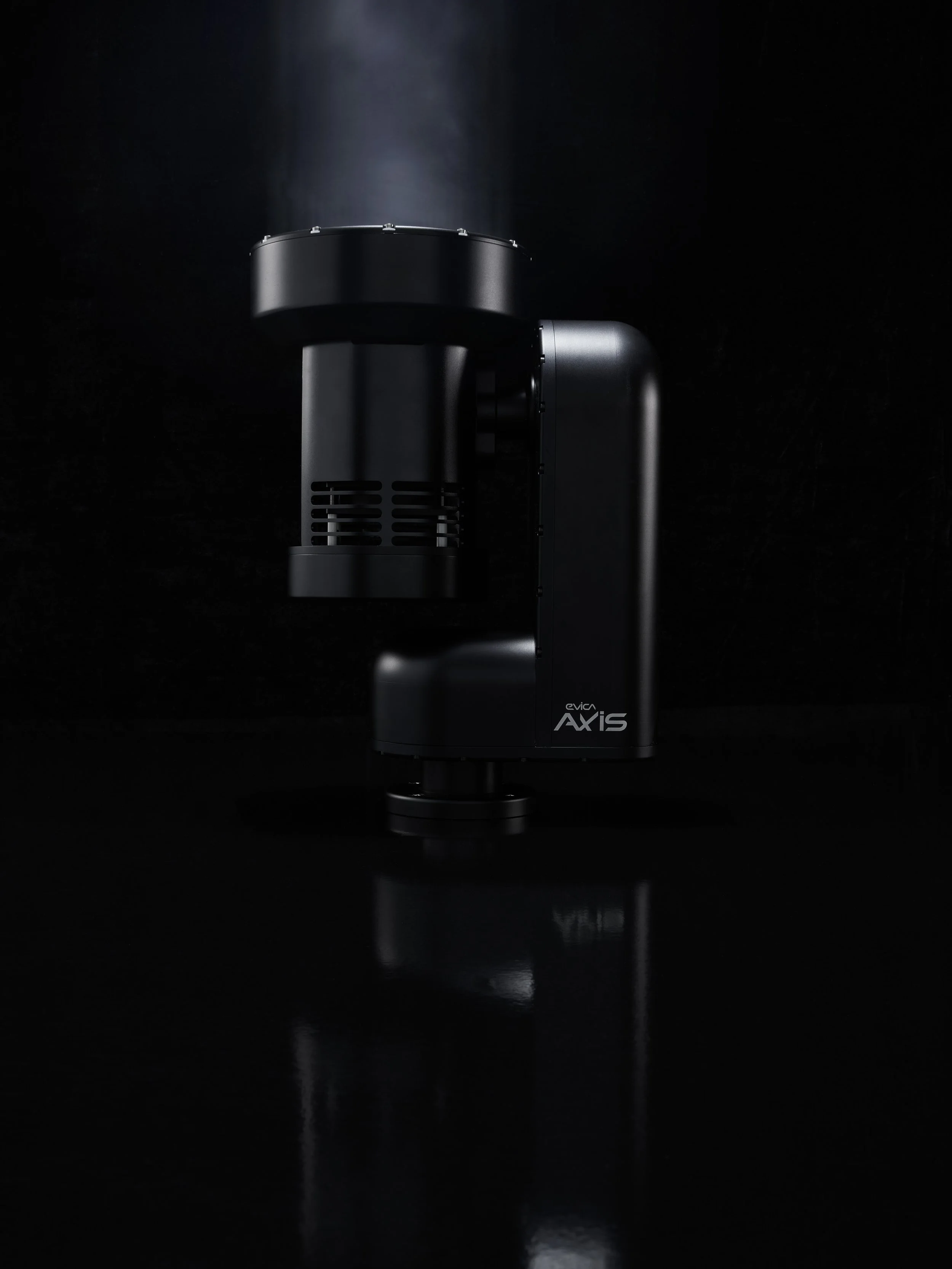Close-up of a black Evica AXIS machine against a dark background, with a beam of light illuminating the top.