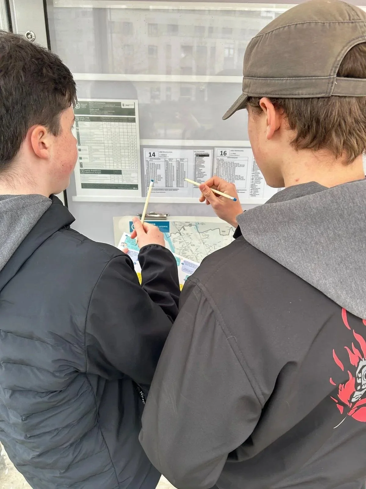 Two young men looking at bus schedule and map at bus stop.