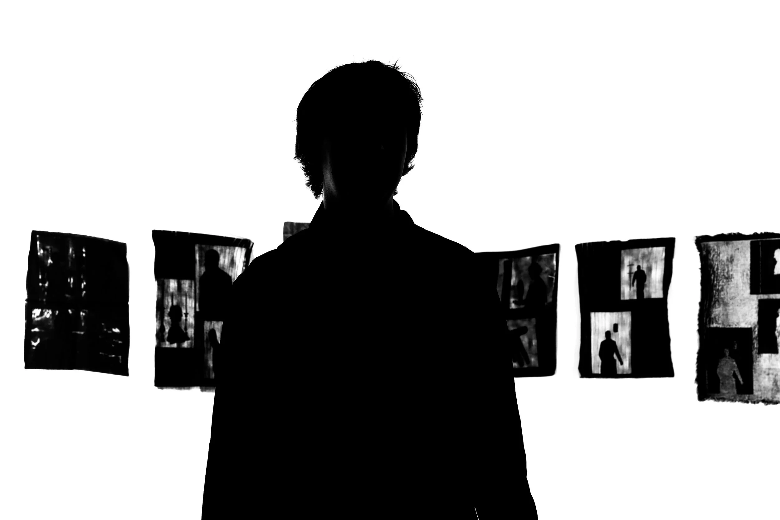 Silhouette of a person standing in front of a wall with several small photographs displayed, with the person facing towards the photos.