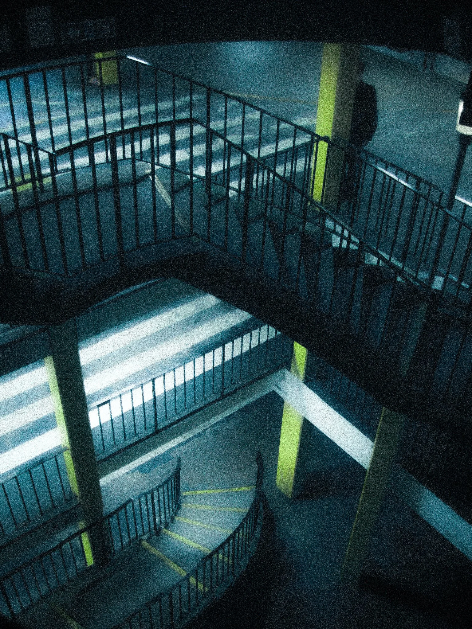 A dark indoor staircase with metal railings and illuminated steps, viewed from above.