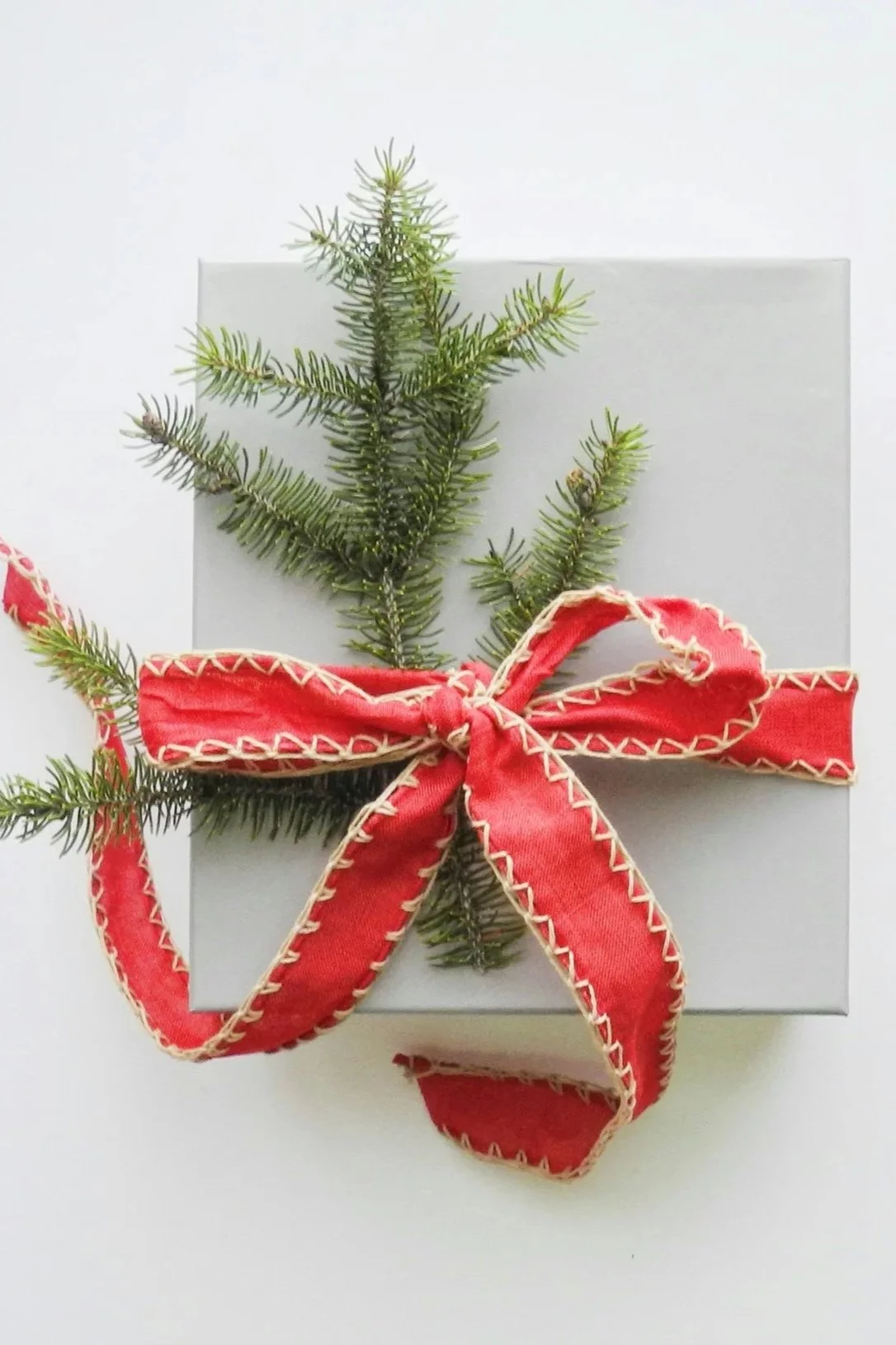 A wrapped Christmas gift with a sprig of evergreen and a red ribbon bow.