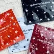 Three small packets of spacemasks in red, blue, and pink colors with star patterns. The packets are on a white surface.