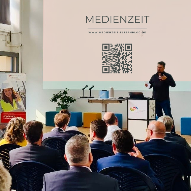 Tobias Dillinger bei einem Medienzeit Vortrag vor Unternehmenspublikum mit Präsentation und QR-Code auf großer Leinwand.