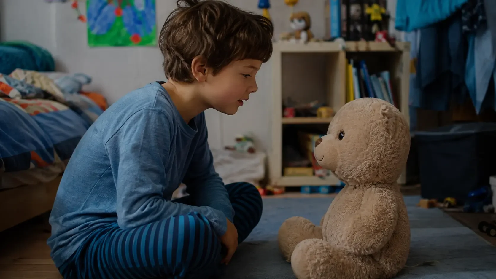 Ein Junge sitzt in seinem Kinderzimmer einem vernetzten KI-Teddybären gegenüber und spricht mit ihm.