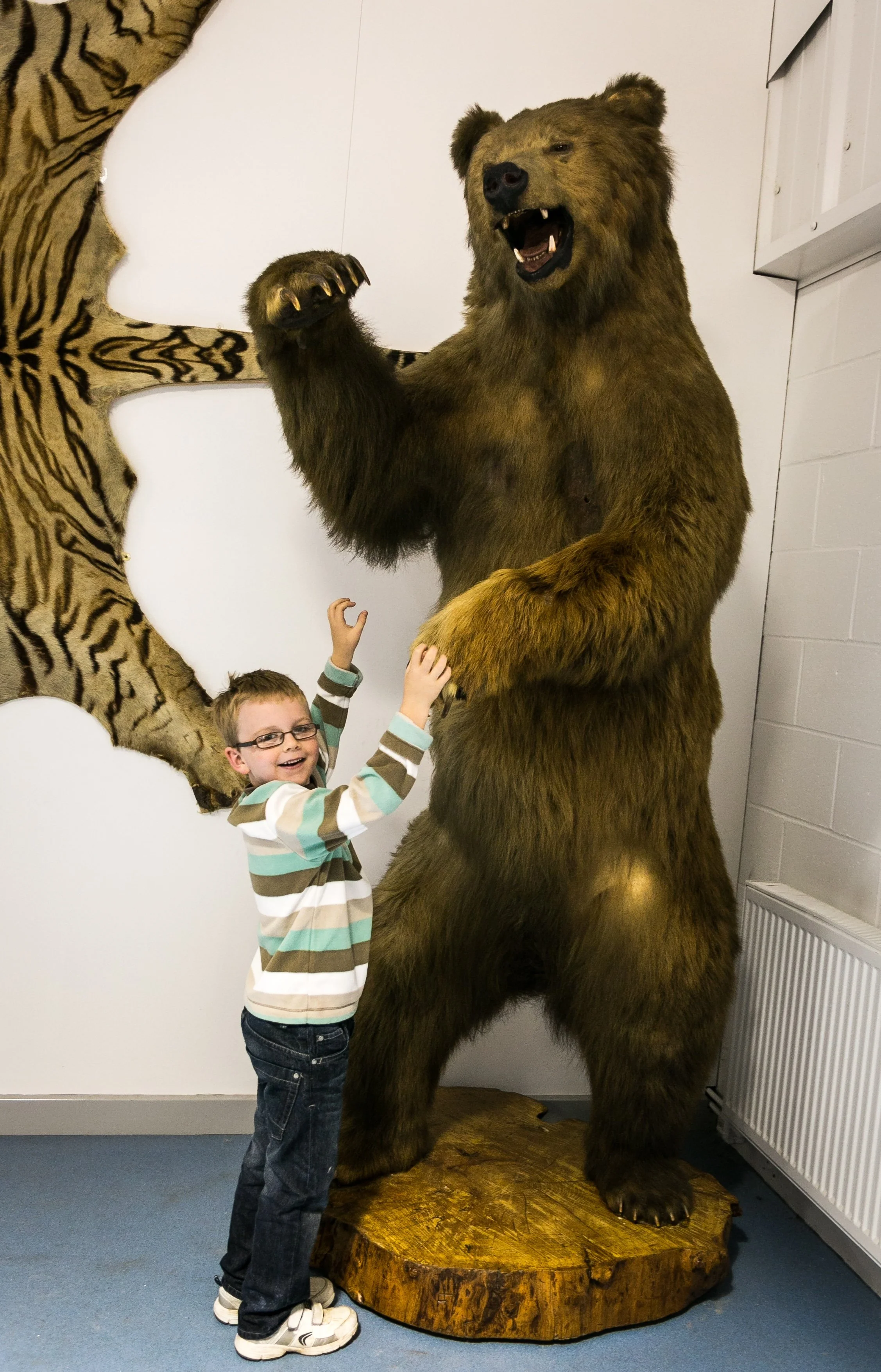 A child standing in front of a large bear statue, waving and smiling.