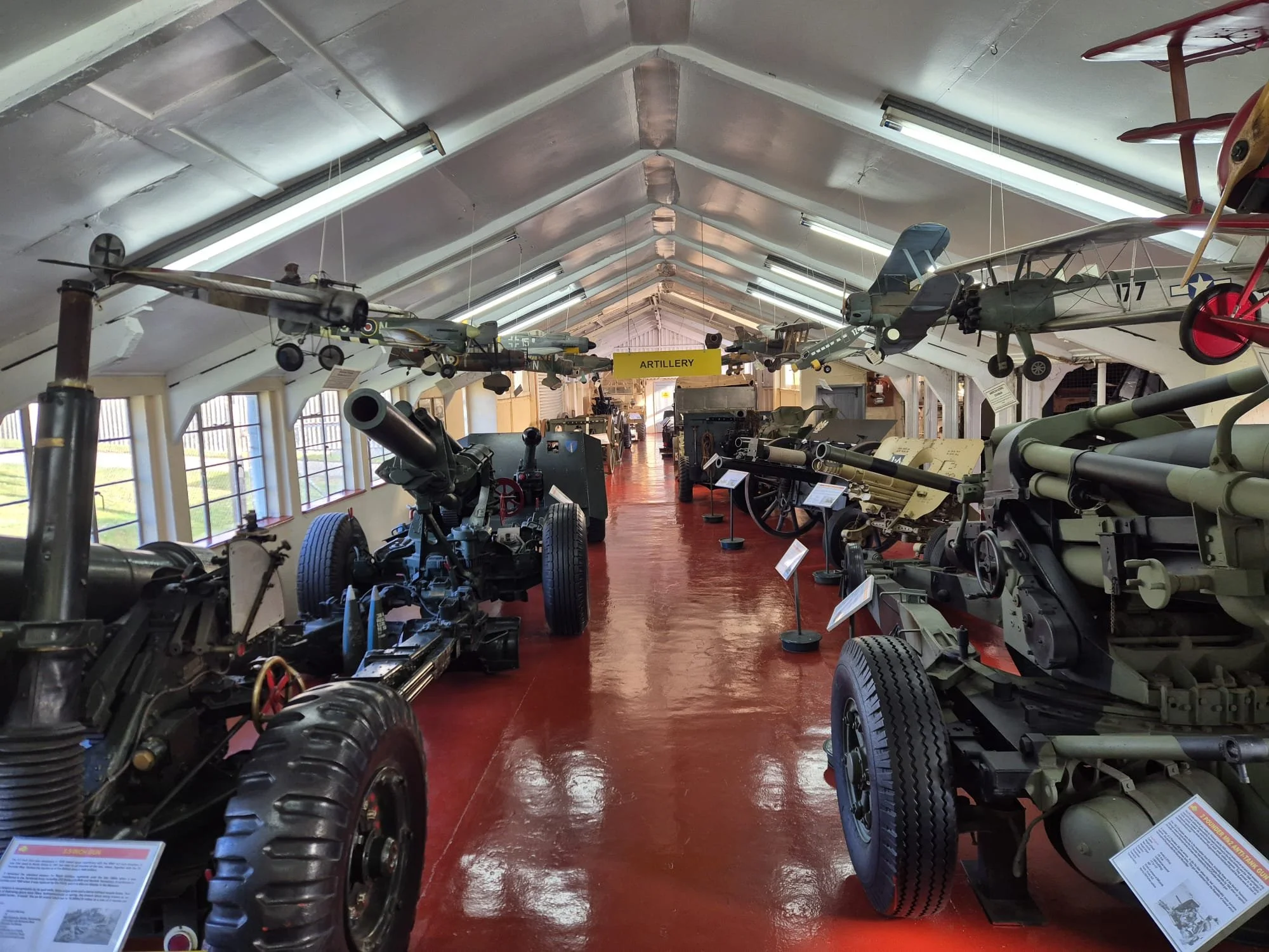 Military artillery and aircraft displayed in a museum with informational signage.