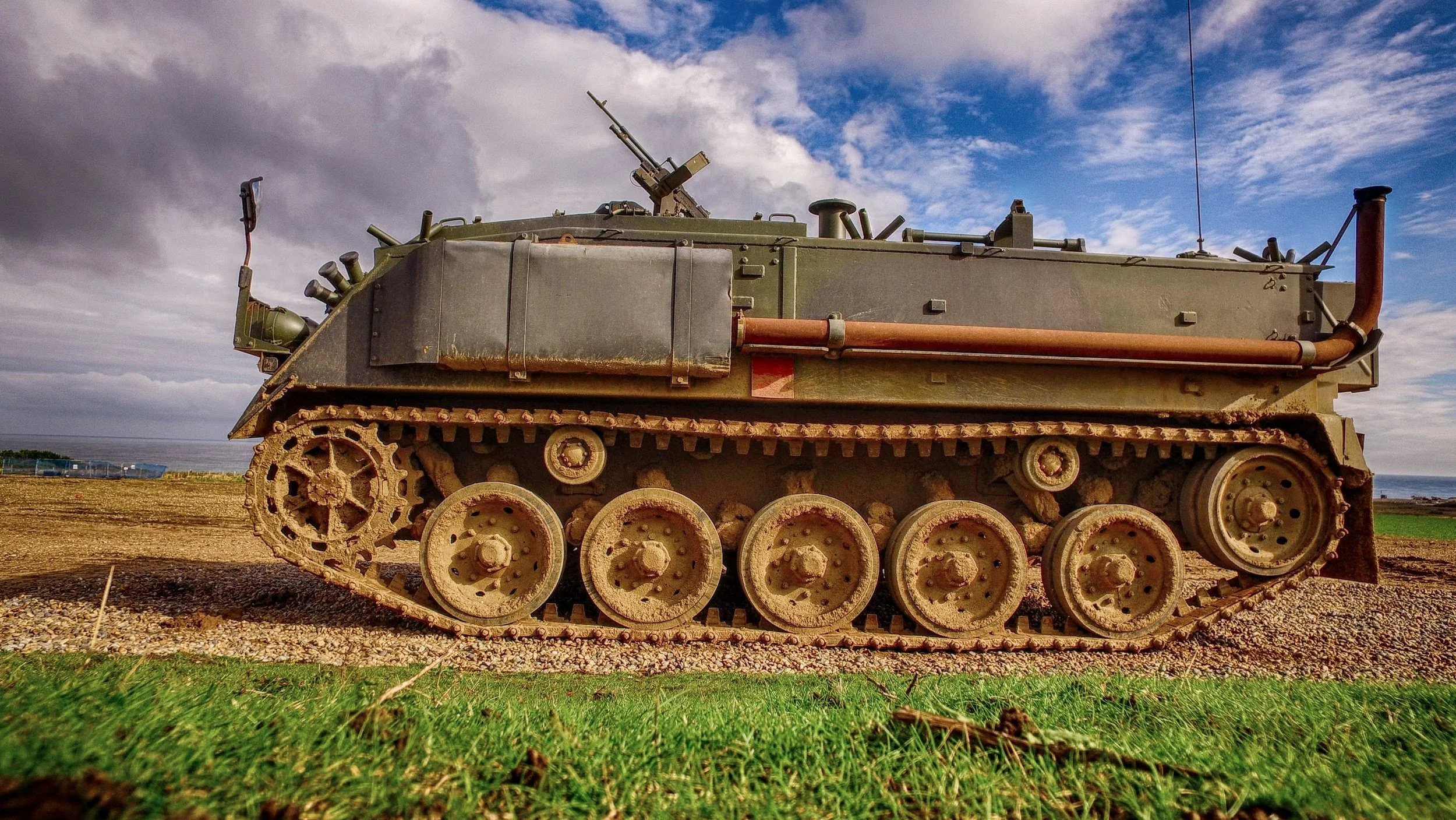 A military tank with rusted tracks on a grassy field, cloudy sky in the background.
