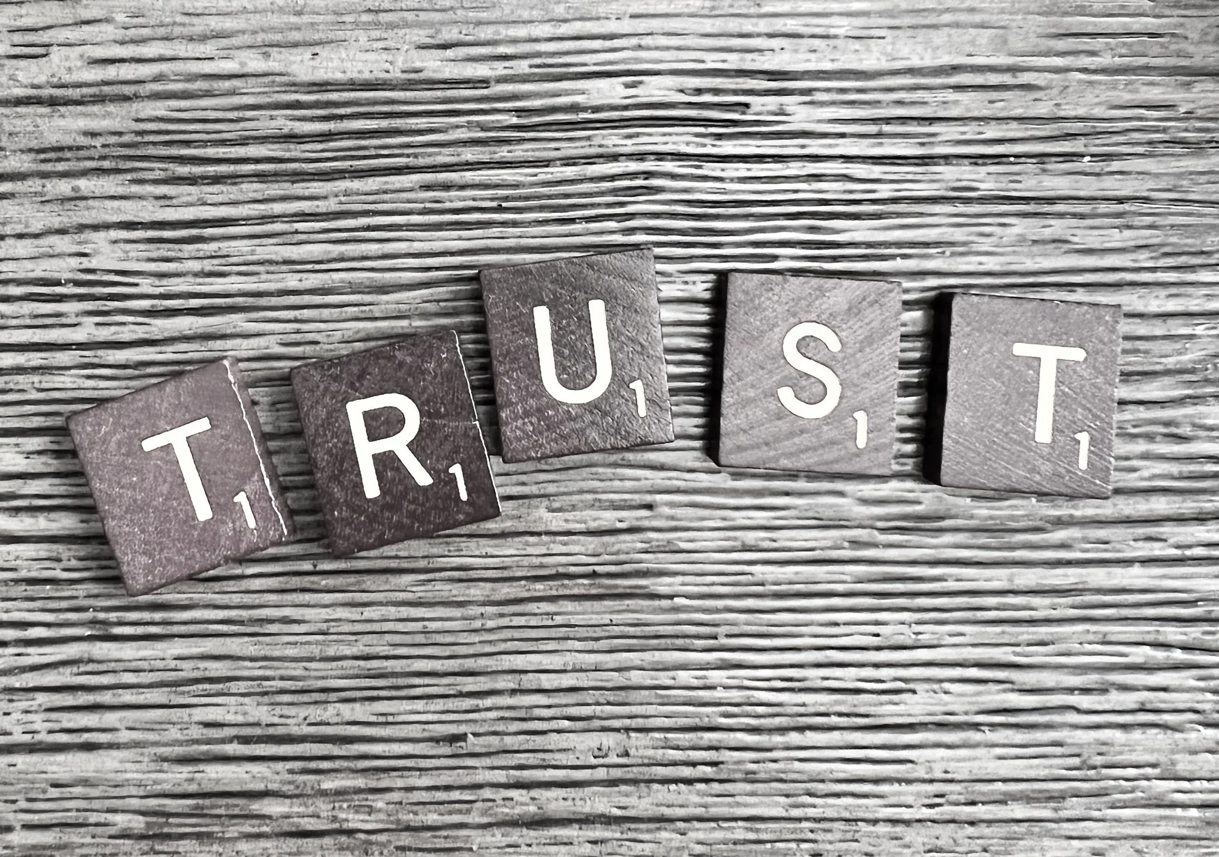 Scrabble tiles spelling out 'TRUST' on a wooden surface.